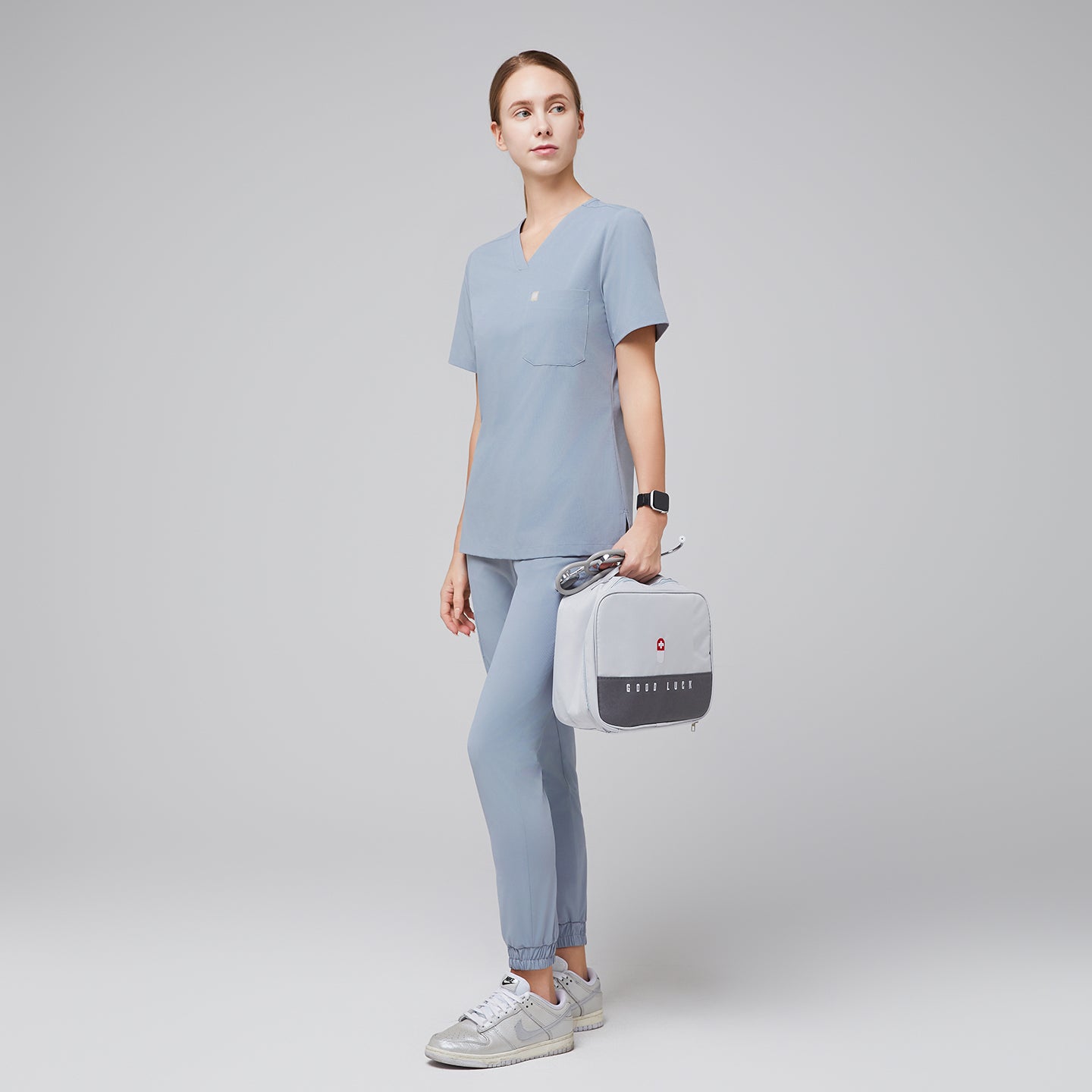 Image of Cool gray single-pocket scrub top Zenir, model wearing with V-neck and short sleeves, full-body view.