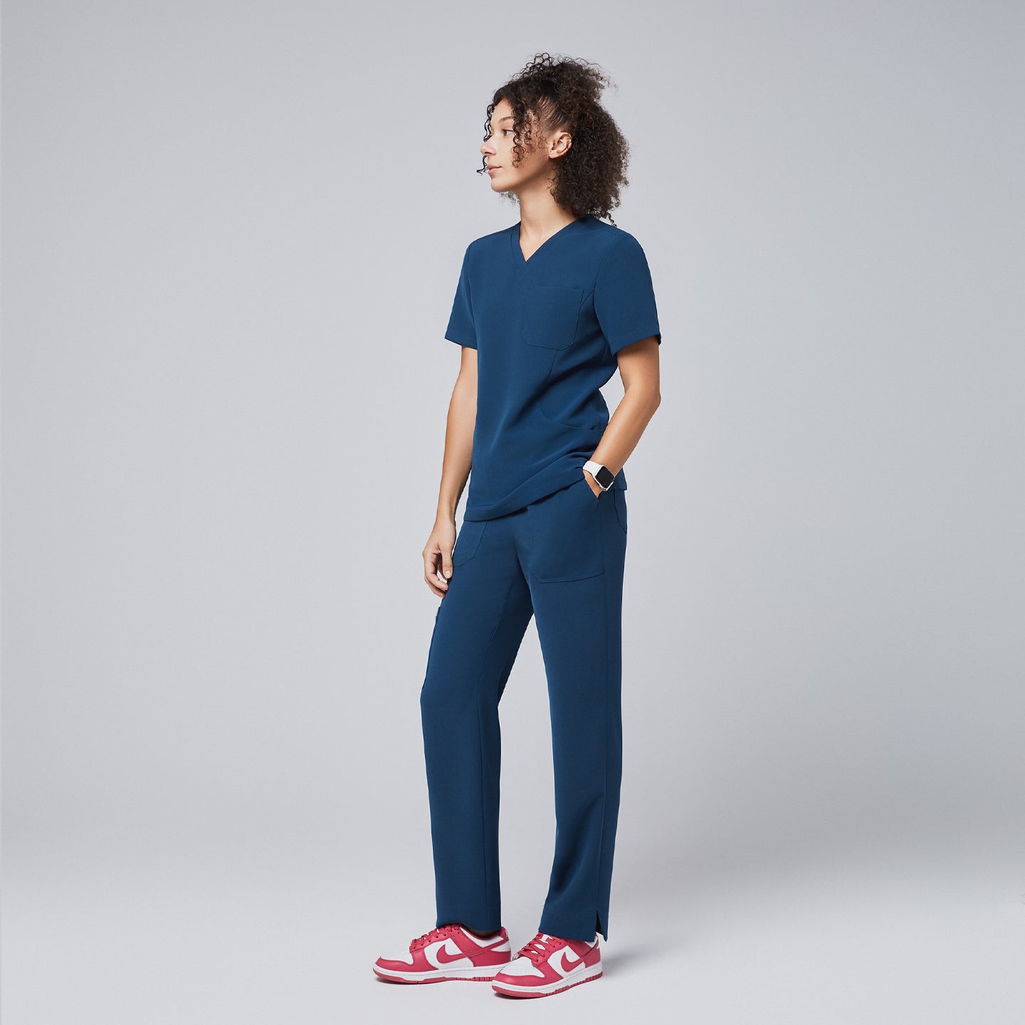 Image of Side view of a woman wearing a dark blue scrub top and pants, paired with red sneakers, demonstrating the professional and comfortable design of the uniform,Dark Blue