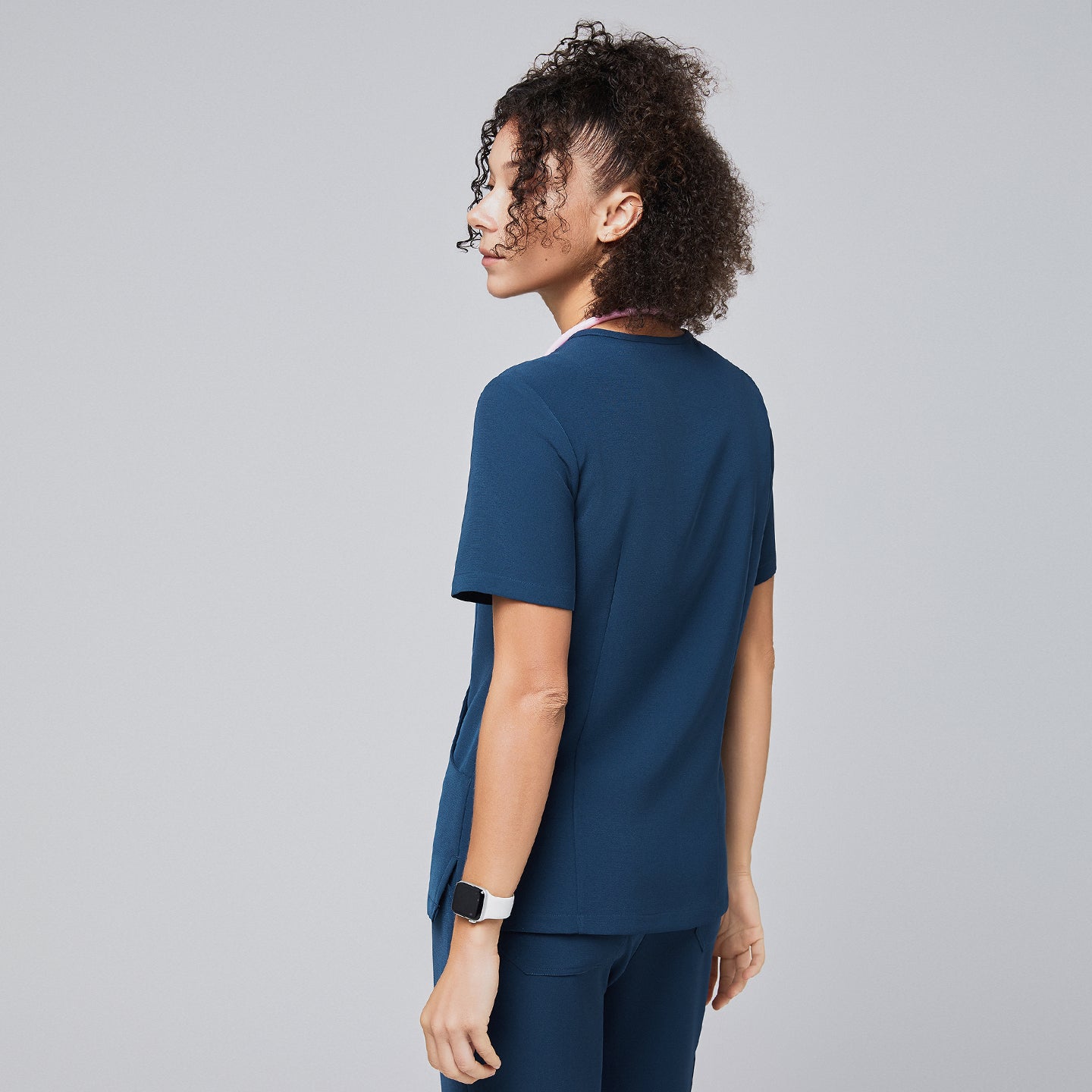 Backside image of a woman wearing a dark blue scrub top and pants, showcasing the fit and design of the clothing, against a light gray background,Dark Blue