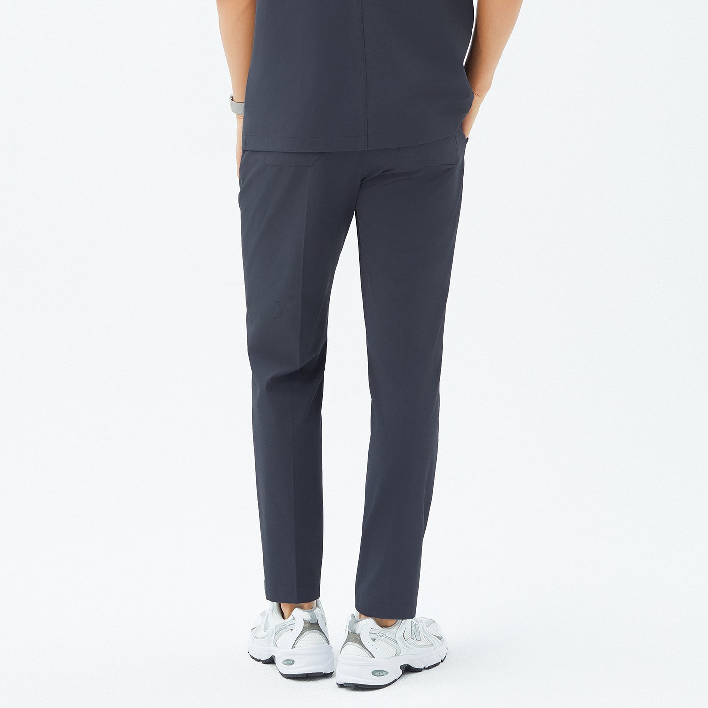 Back angle of TUL Men’s Premium Banding Pants in Deep Gray, showing the model’s left pocket and center back seam. The matching scrub top aligns at the waist, and the model wears white sneakers.