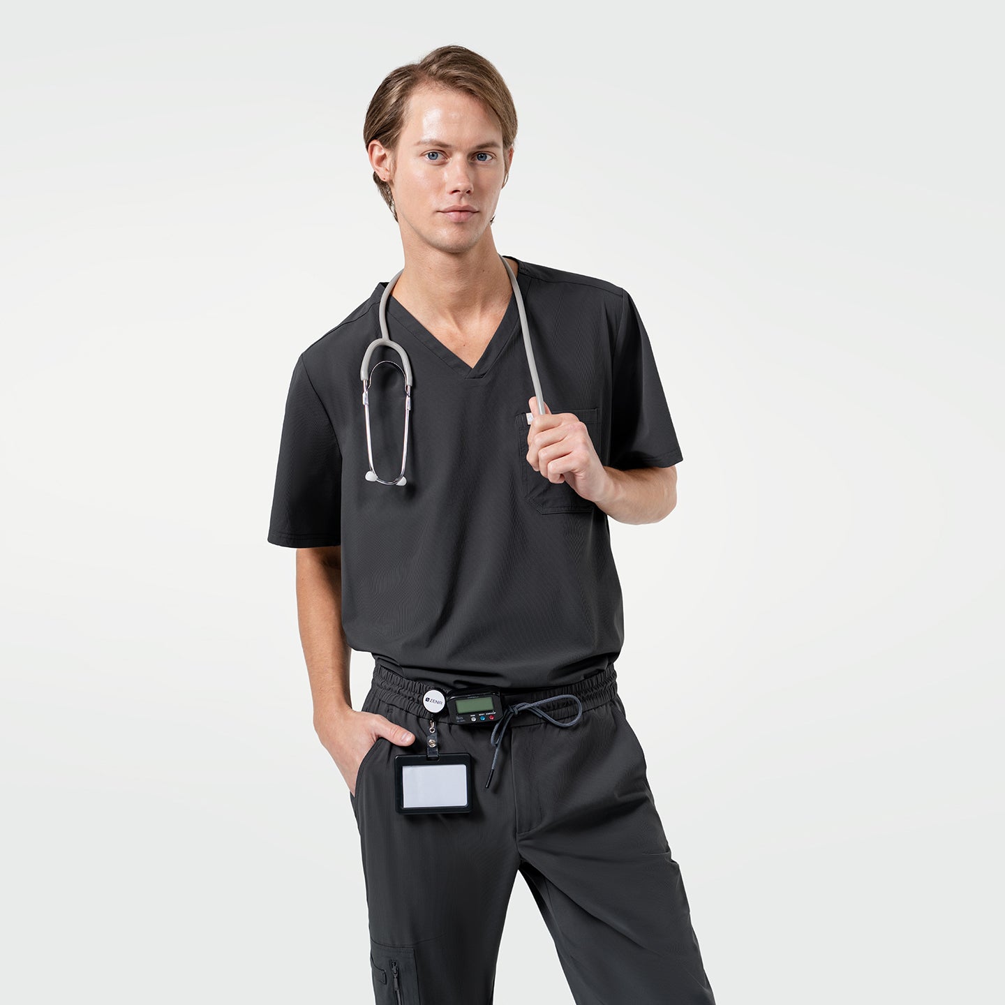 Image of Styled in the Deep Gray Single Pocket Scrub Top, the model maintains a relaxed stance with the stethoscope in hand and one hand resting in the pocket.