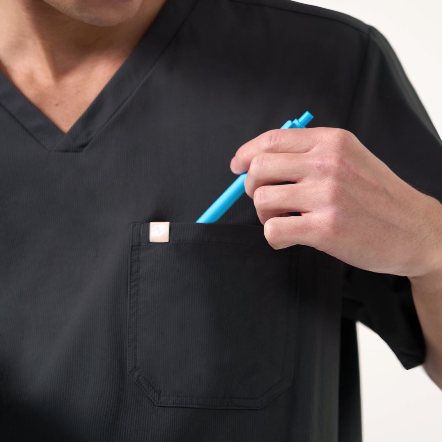 Image of A close-up shows the model slipping a blue pen into the pocket of the Deep Gray Single Pocket Scrub Top.