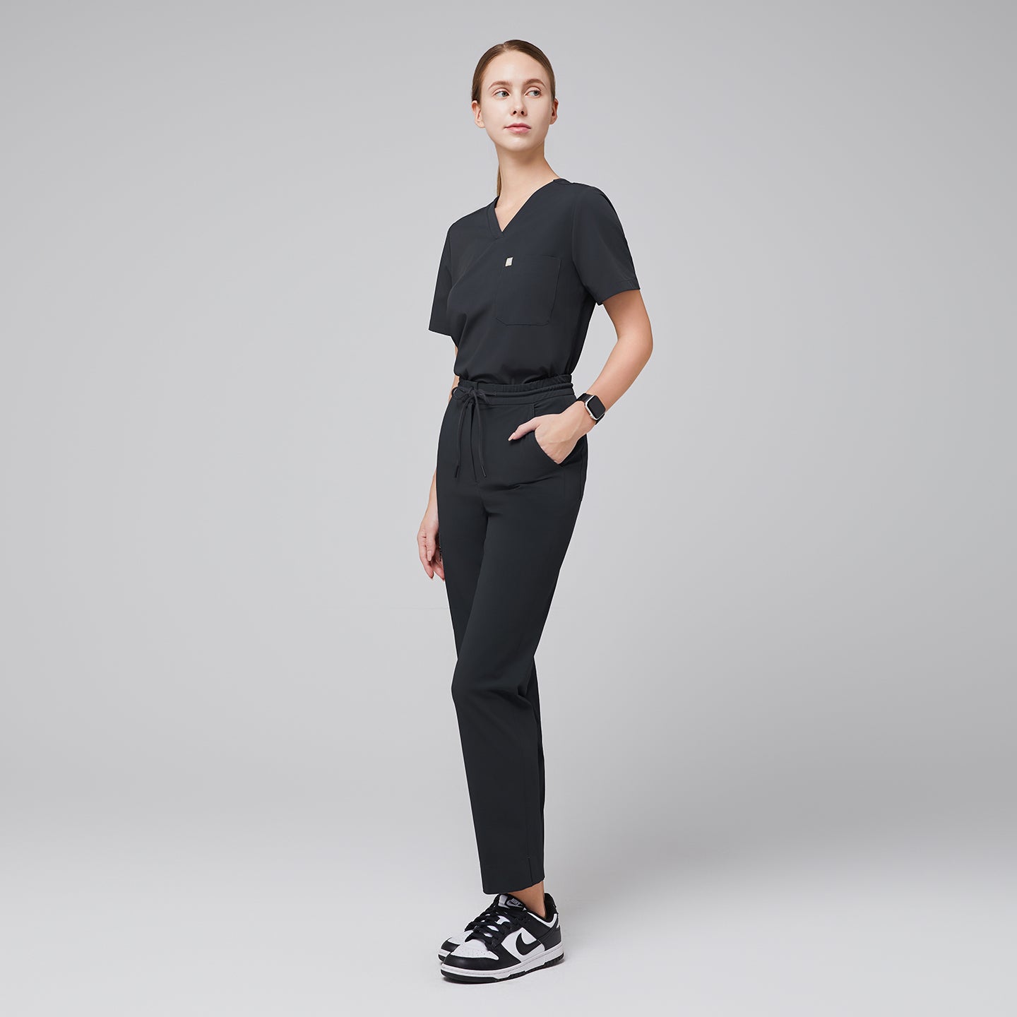Image of Professional scrub set with a V-neck top and drawstring pants featuring zipper pockets and split hem, paired with sneakers for a sleek, modern look,Deep Gray