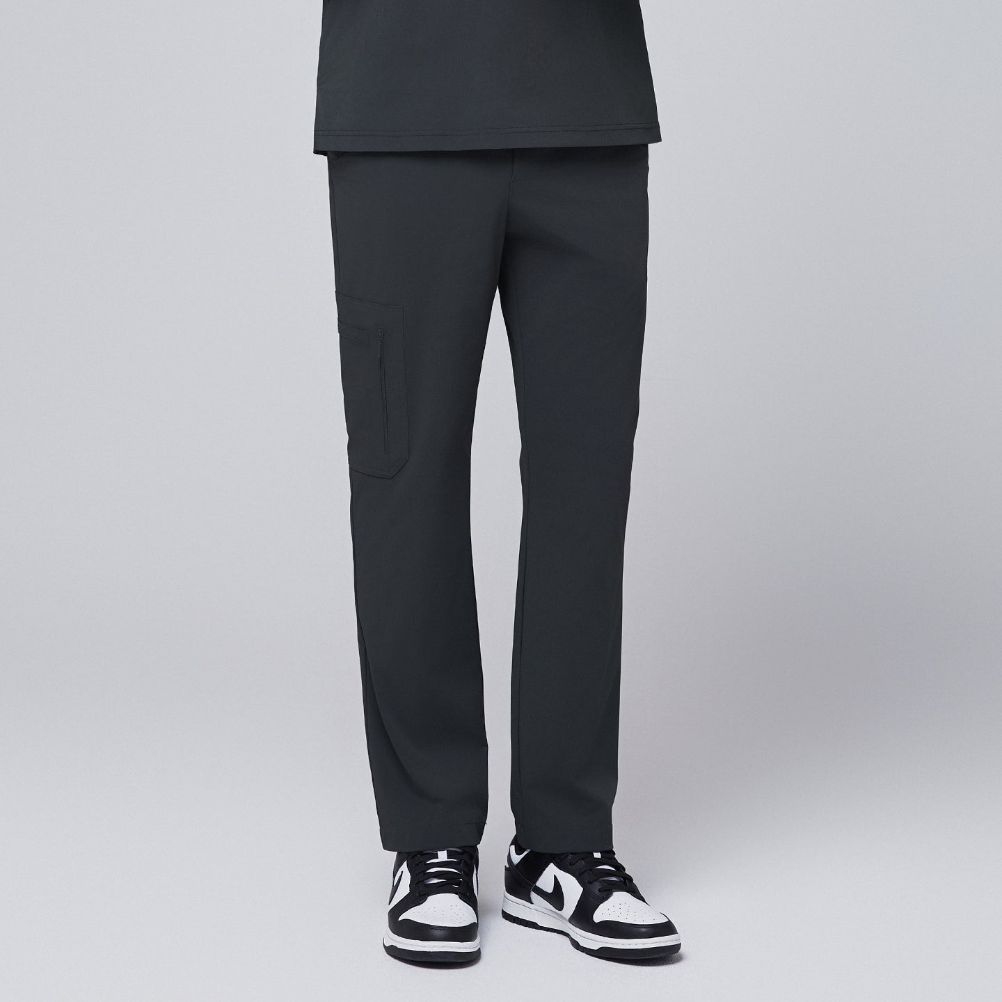 Image of Front view of deep gray scrub pants featuring a sleek zipper pocket on the side, paired with black and white sneakers, modeled against a neutral gray background,Deep Gray