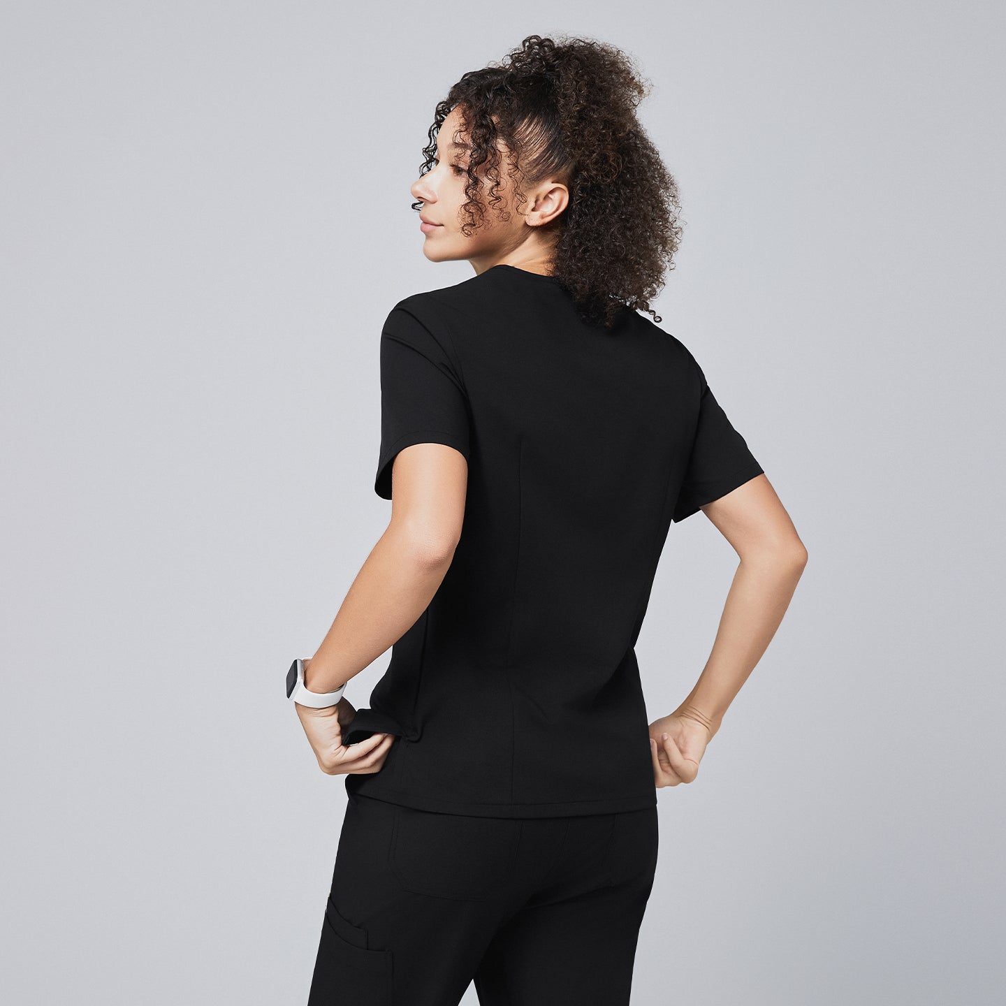 Image of Woman showcasing the back design of a black scrub top with short sleeves, paired with matching scrub pants,Eco Black