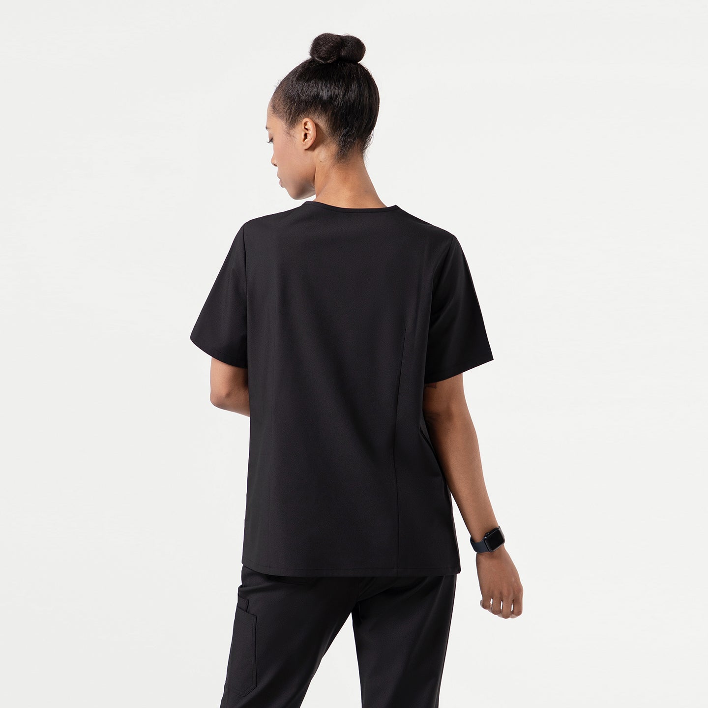 Image of A person shown from the back wearing an Eco Black scrub top with short sleeves, displaying the clean and minimal back design.