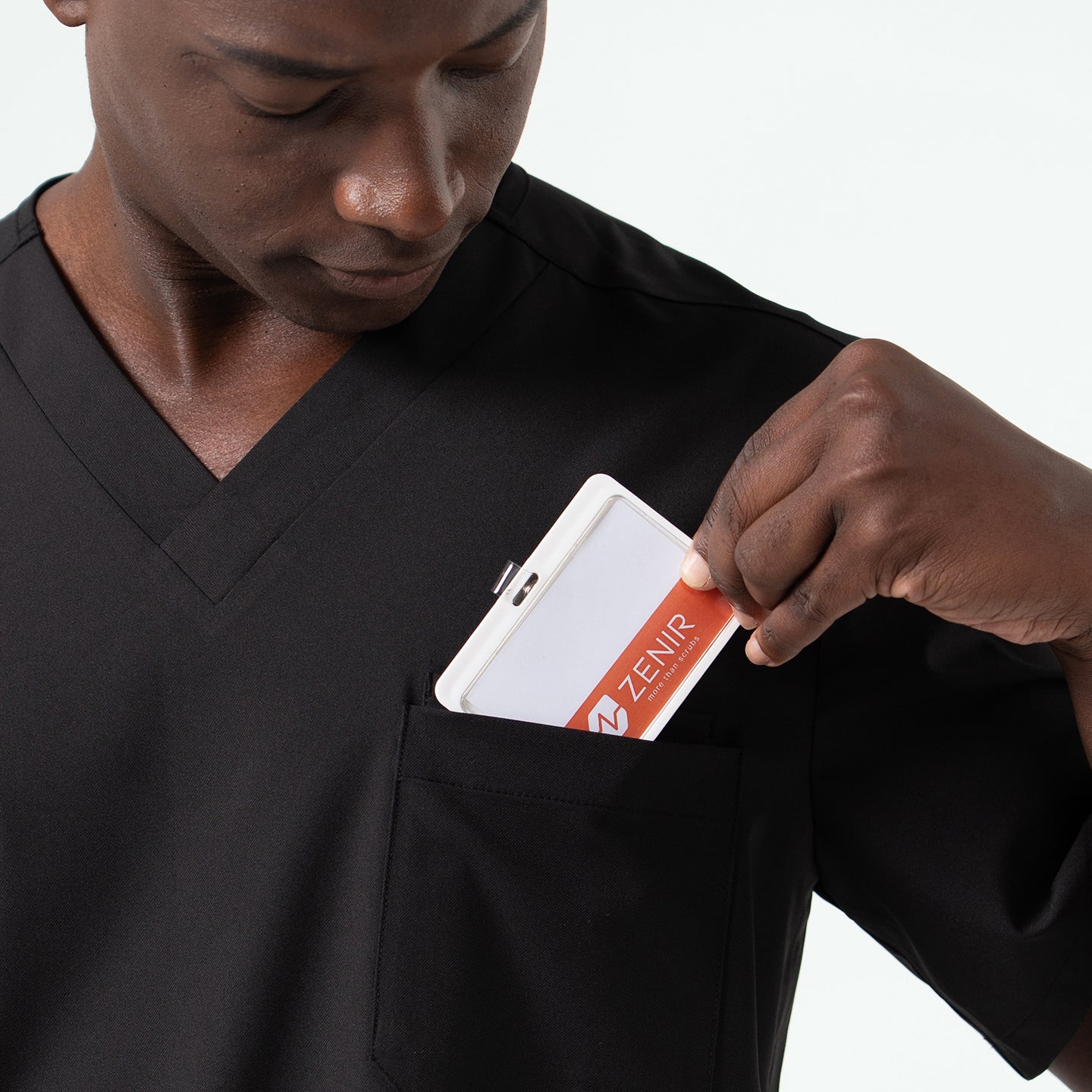 Image of Close-up of a medical professional placing a ID badge into the chest pocket of an Eco Black scrub top, highlighting the secure pocket design and smooth fabric texture.