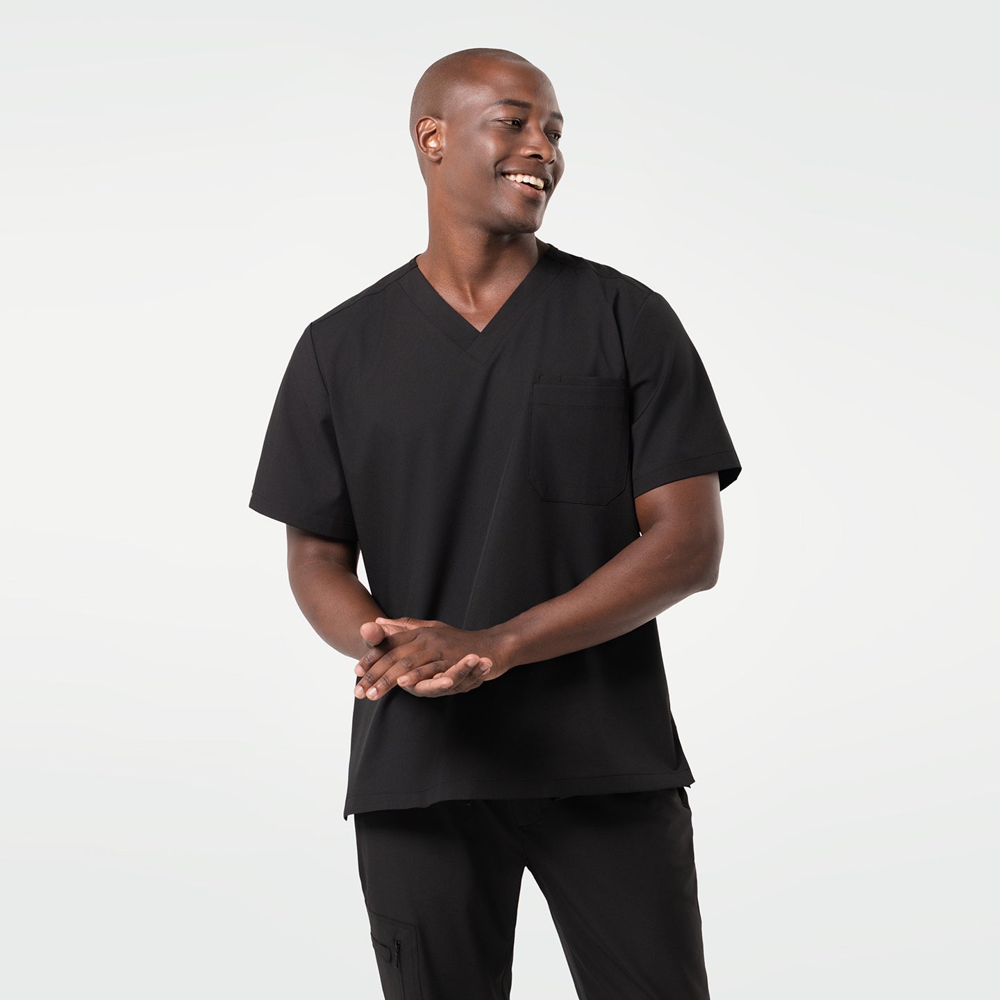 Image of A smiling male model wearing a short-sleeve 3 Pocket scrub top in Eco Black.