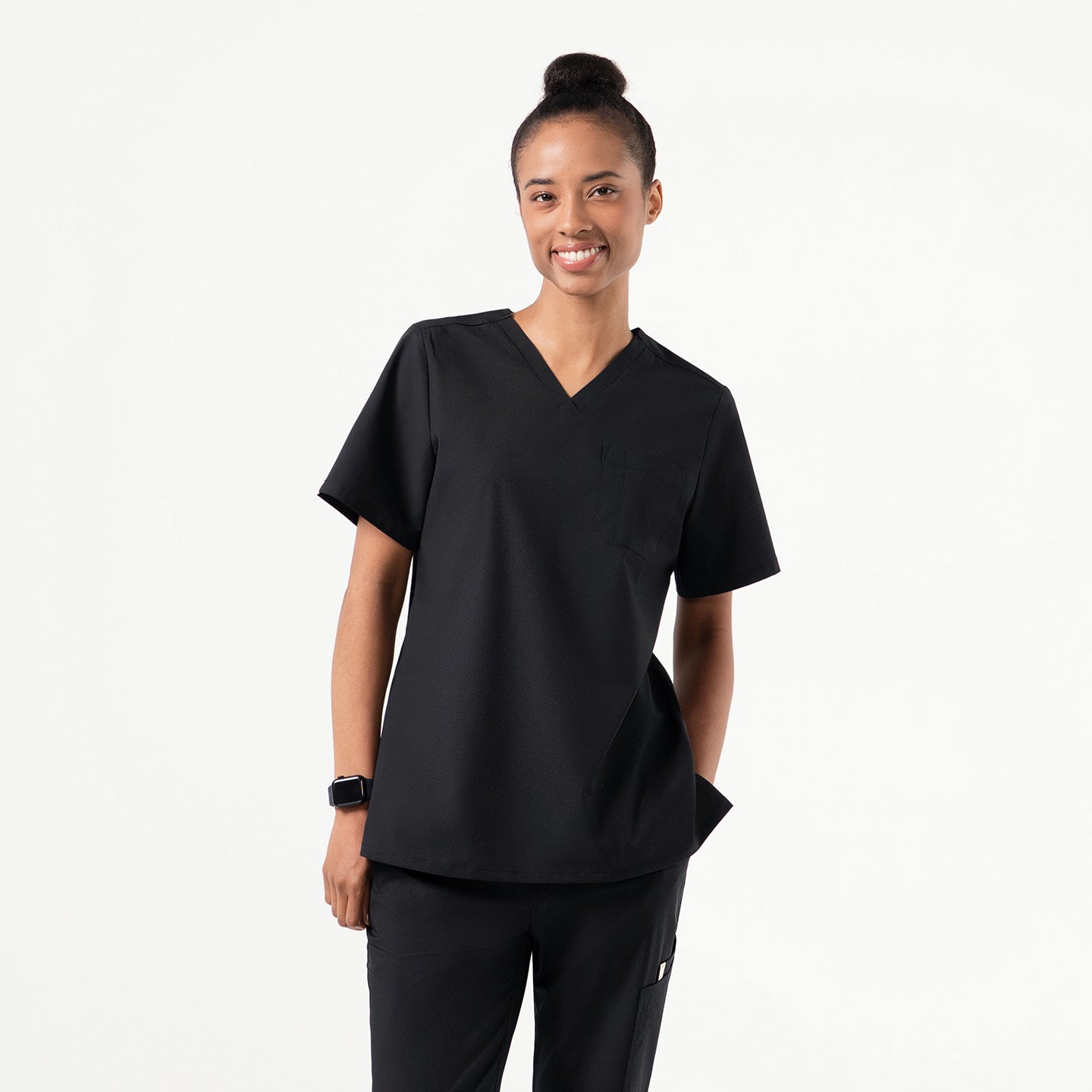 Image of A person wearing an Eco Black V-neck scrub top with a three-pocket design, standing with a relaxed smile and one hand in the side pocket.