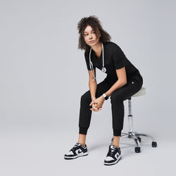 Image of Woman wearing a black scrub set with a stethoscope, sitting on a stool in a relaxed pose,Eco Black