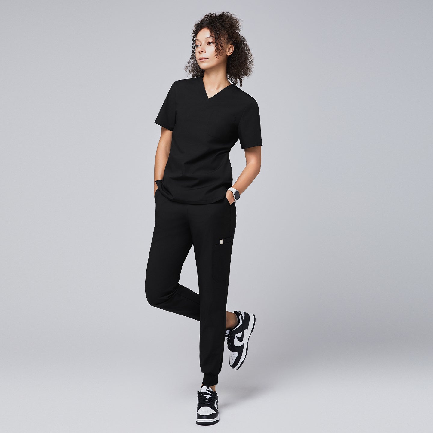 Woman wearing a black scrub top and jogger-style scrub pants, paired with sneakers, standing confidently,Eco Black