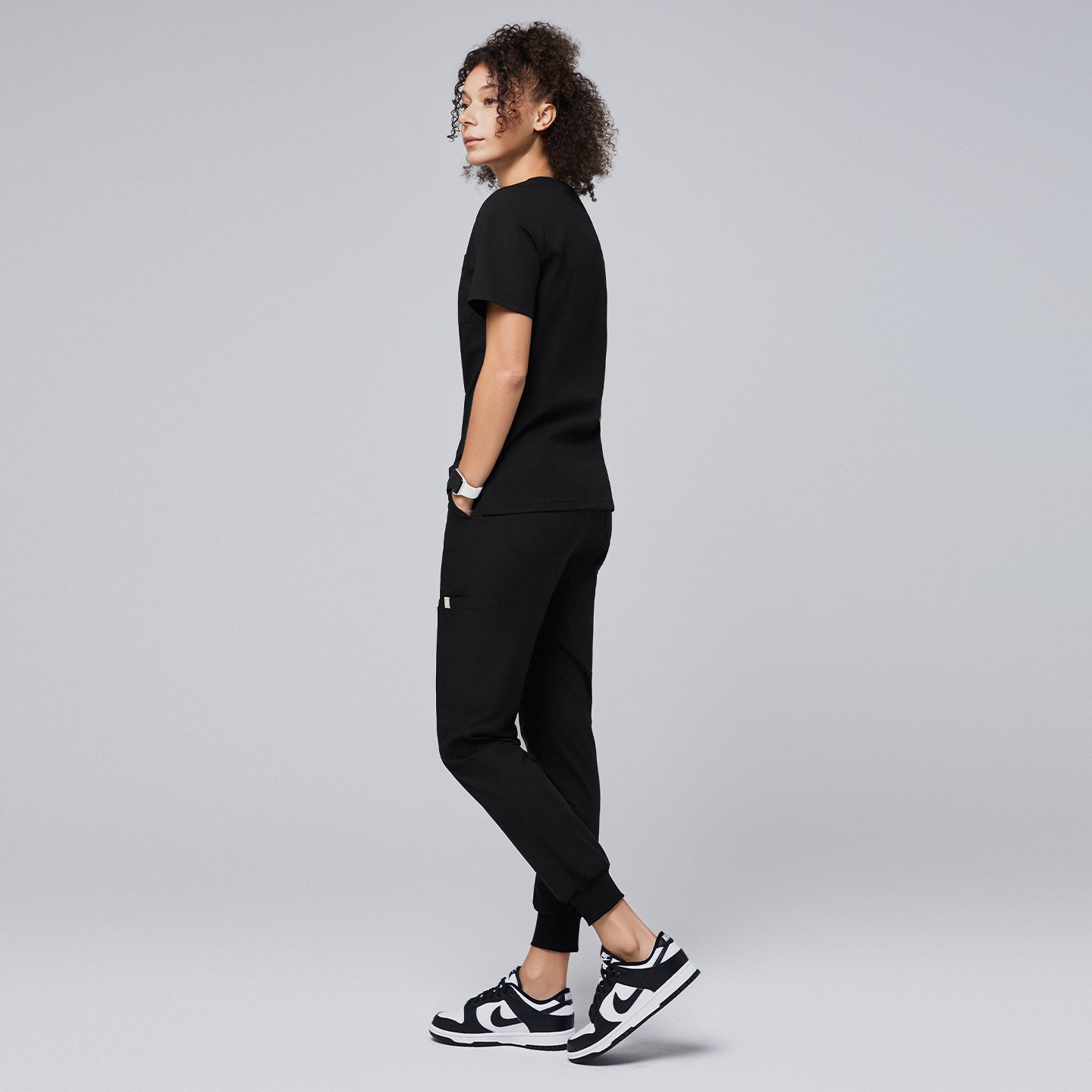 Image of Woman wearing a black scrub set with jogger-style pants and sneakers, standing in a side profile pose,Eco Black