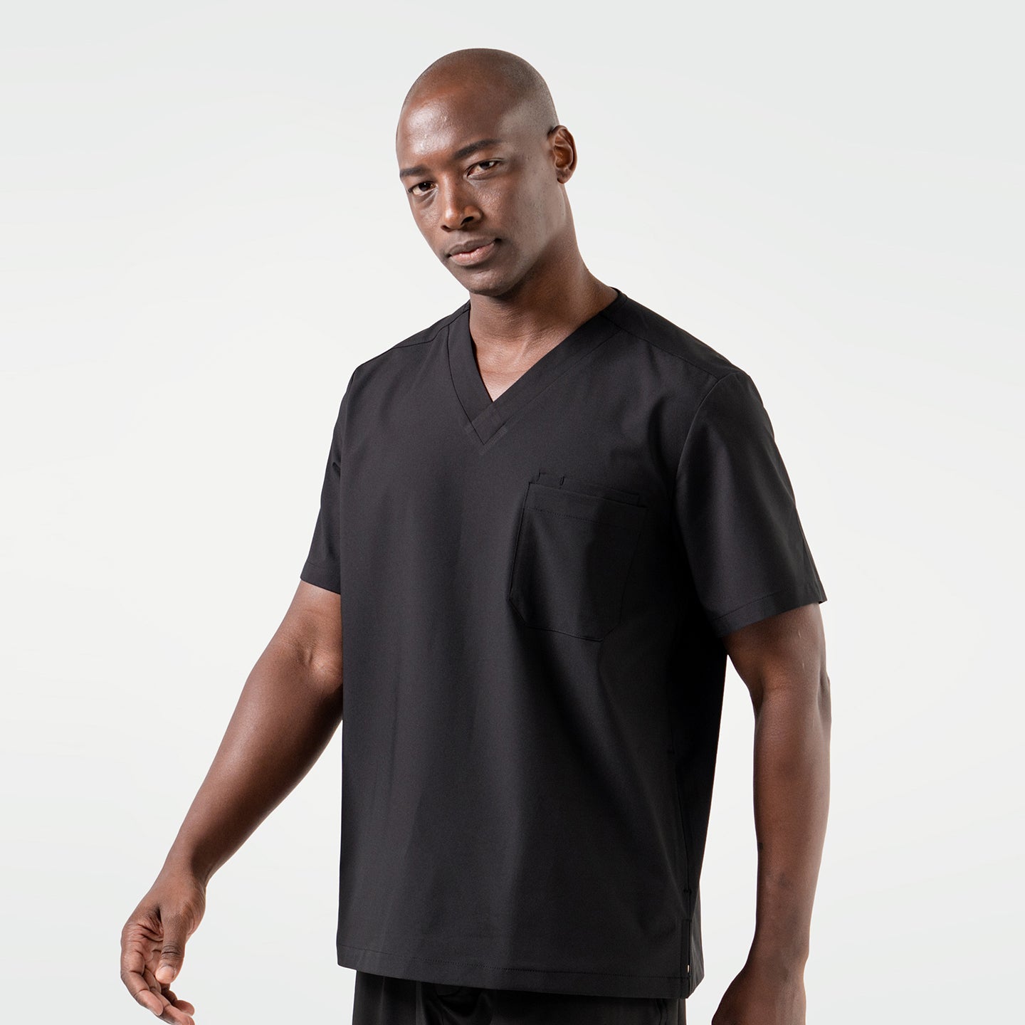A smiling male model dressed in an Eco Black 3 Pocket scrub top, standing in a relaxed pose.