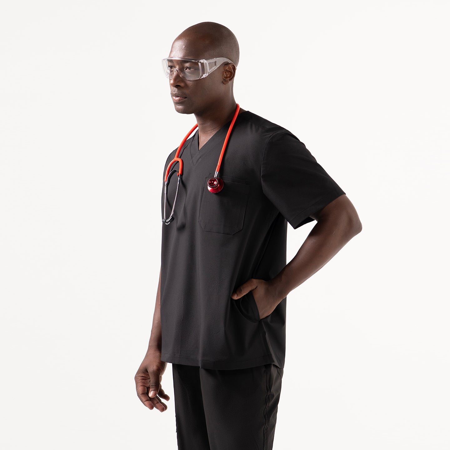 Image of Model wearing an Eco Black V-neck scrub top with three functional pockets, styled with black scrub pants and protective eyewear while holding a confident stance.