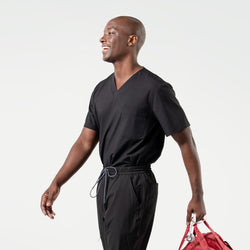 Image of Smiling model in an Eco Black 3 pocket scrub top with short sleeves and chest pocket, paired with matching scrub pants while carrying a red duffel bag.