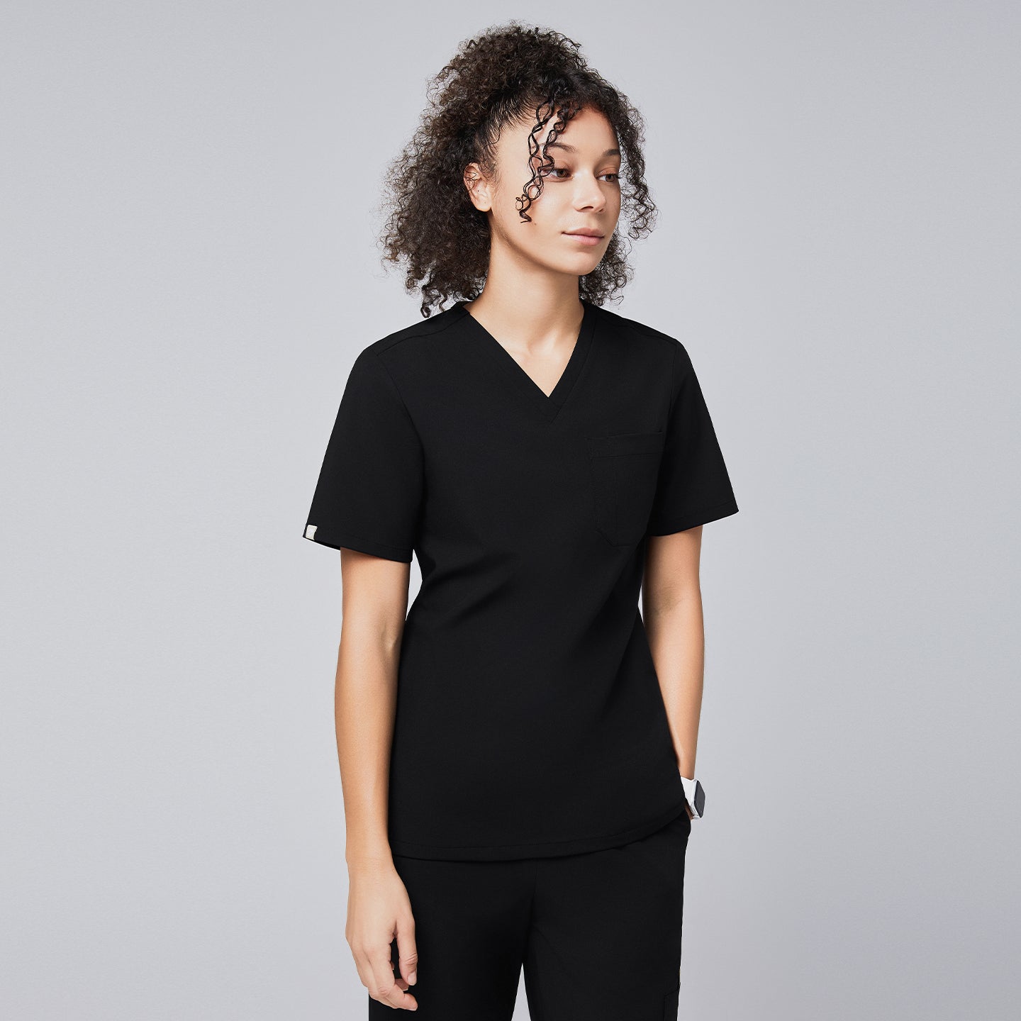 Image of A woman wearing a black eco-friendly scrub top with a V-neck design and a chest pocket, styled with matching black scrub pants,Eco Black