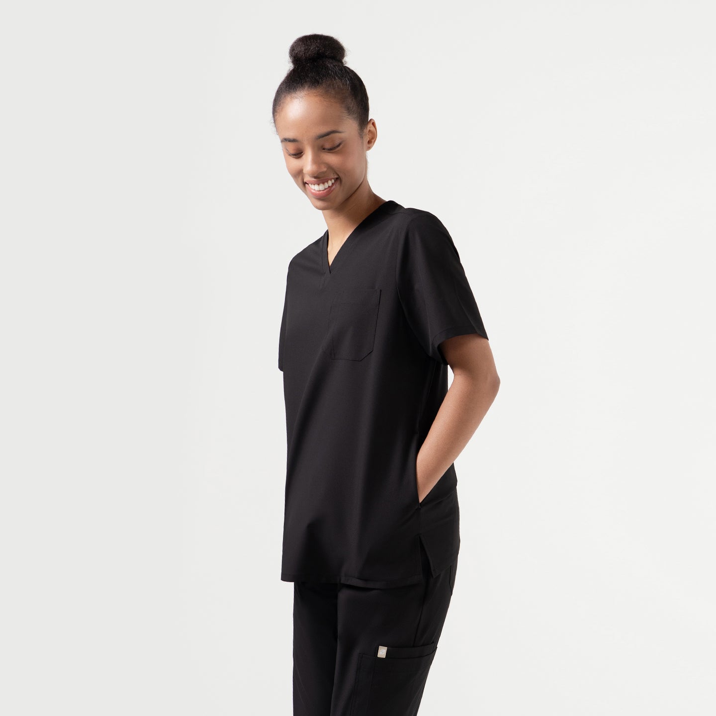 Model wearing the Eco Black 3-Pocket Scrub Top in a relaxed side pose, showing the V-neckline and chest pocket.