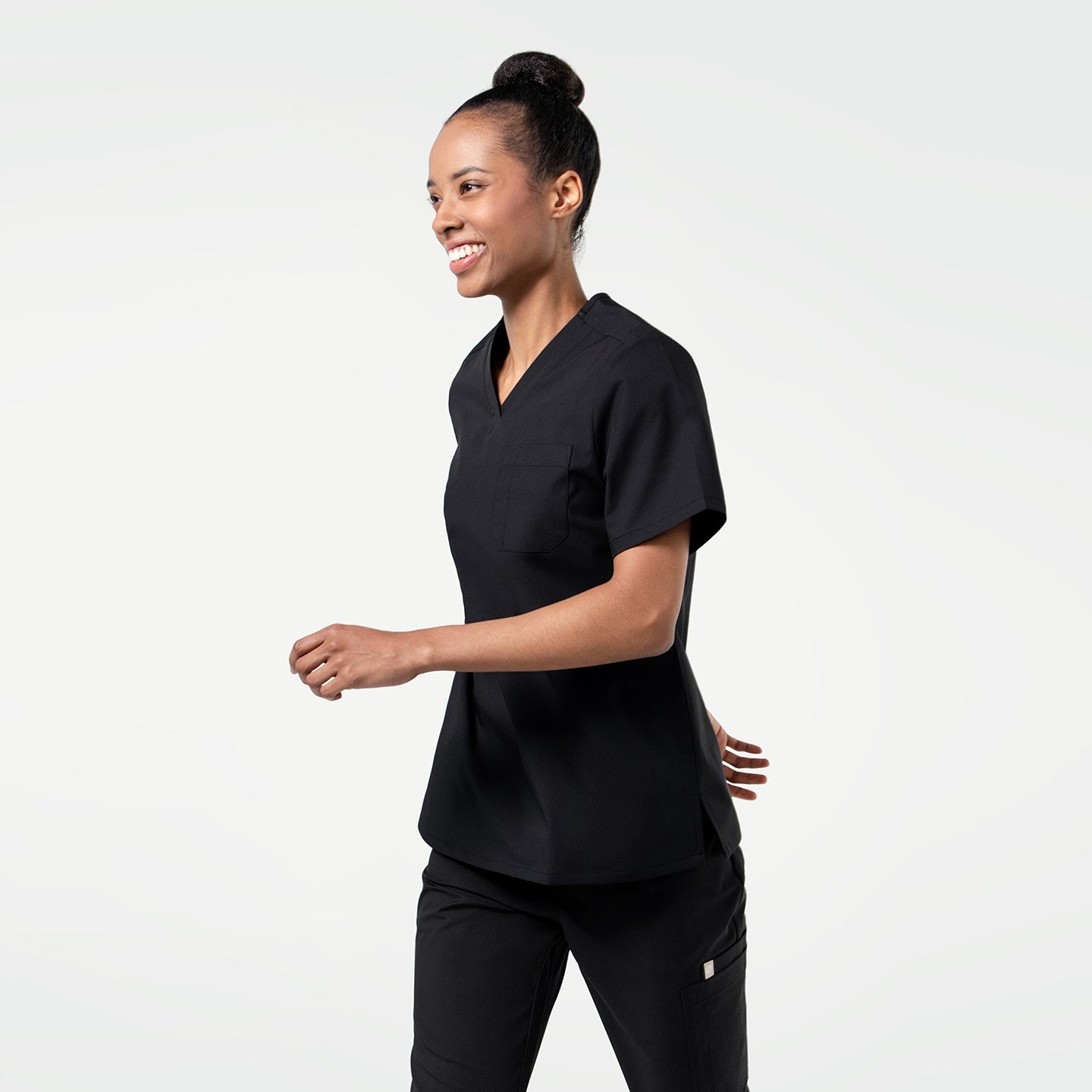 Image of Eco Black 3 Pocket Scrub Top in a candid walking pose, captured mid-motion with a bright smile for a natural and energetic vibe.