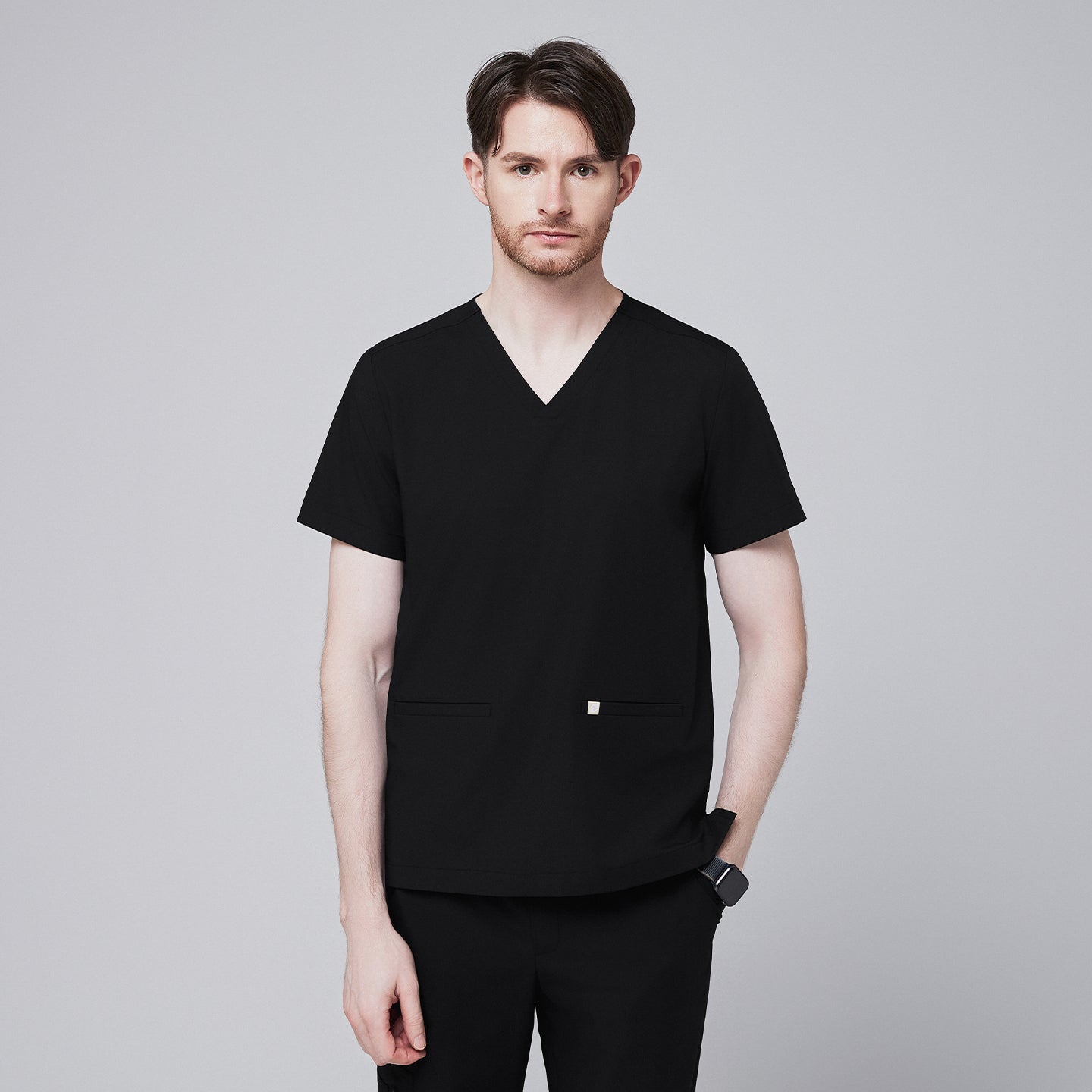 Image of A man wearing an Eco Black Double Pocket Scrub Top with a V-neck and short sleeves,Eco Black