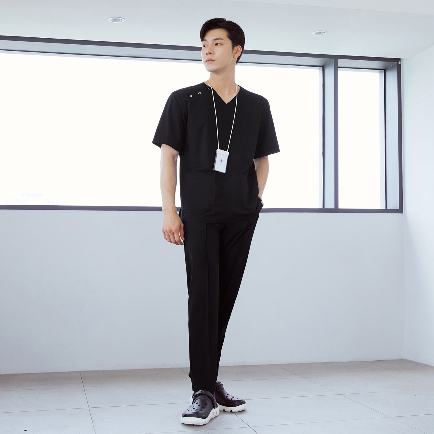 Image of  Man wearing front zipper scrub top with chest and side pockets, paired with banding scrub pants, standing indoors with hands in pockets,Eco Black
