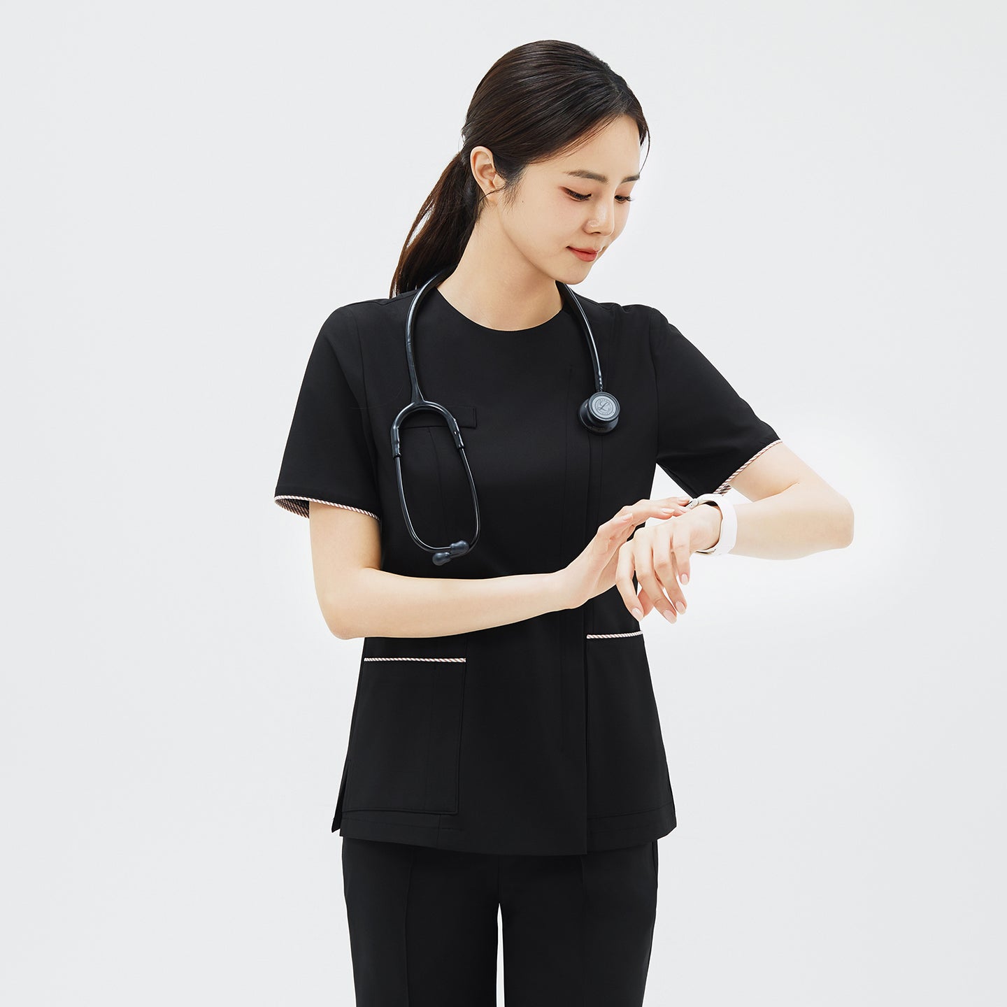 Model checking her watch while wearing TUL OS-206 Women's Edge Stripe Scrub Top in Eco Black, demonstrating comfort and mobility.