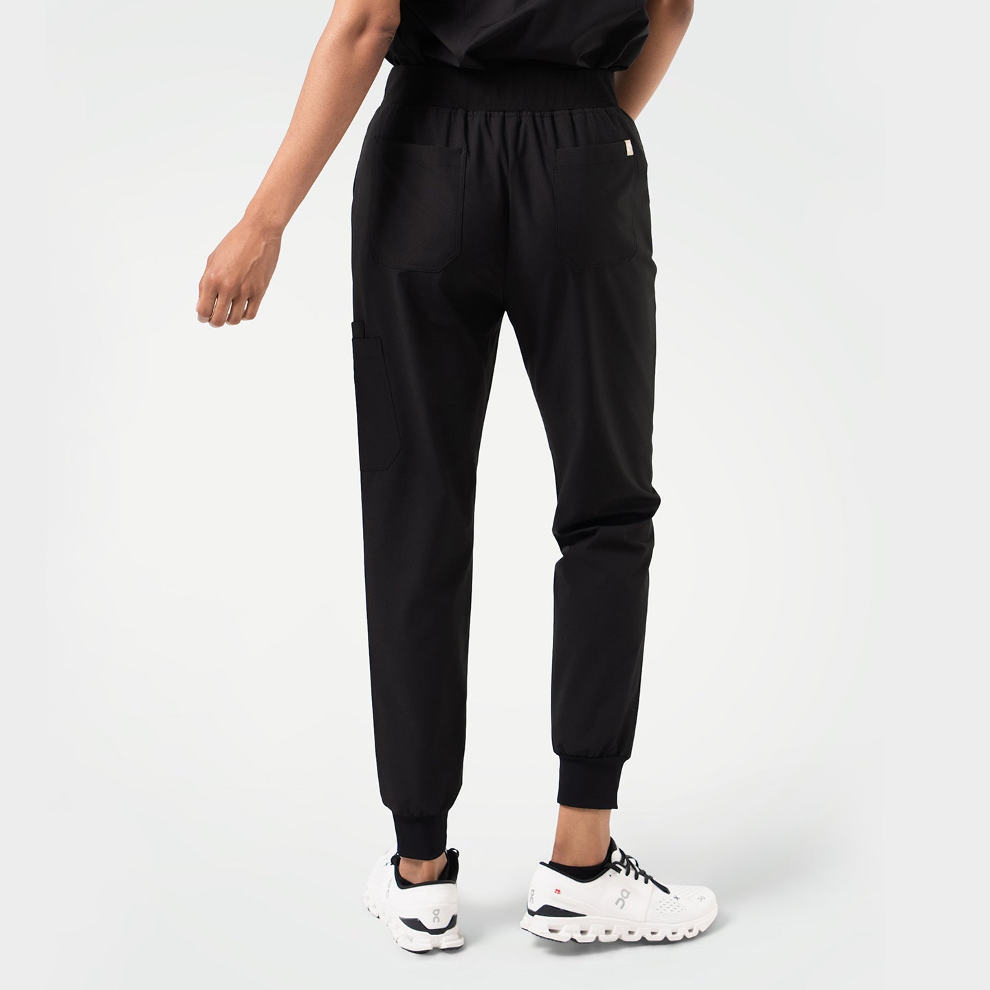 Model wearing eco-black jogger scrub pants viewed from the back, highlighting the relaxed fit and functional pockets.