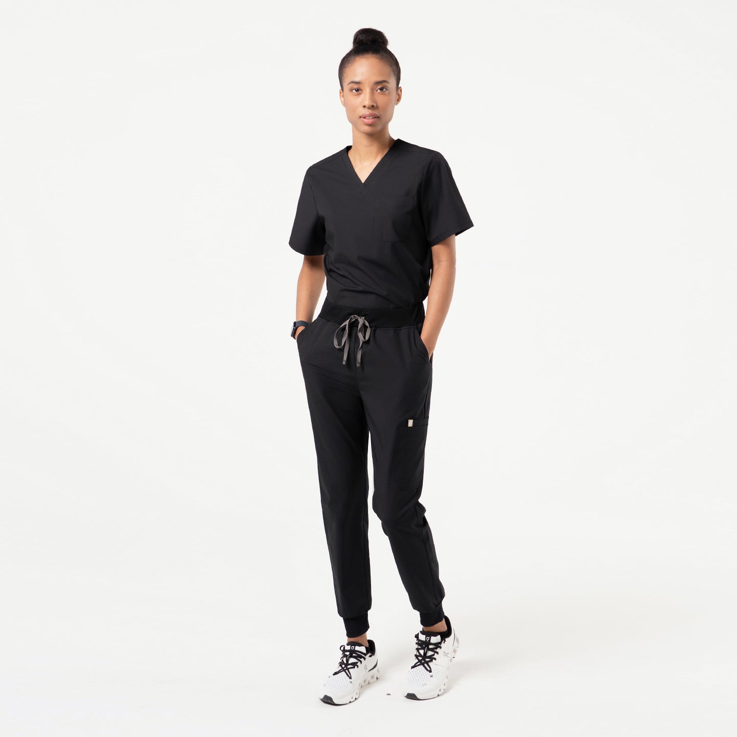 Image of Model wearing Eco-Black jogger scrub pants with back patch pockets and tapered cuffed legs in a minimal studio setting
