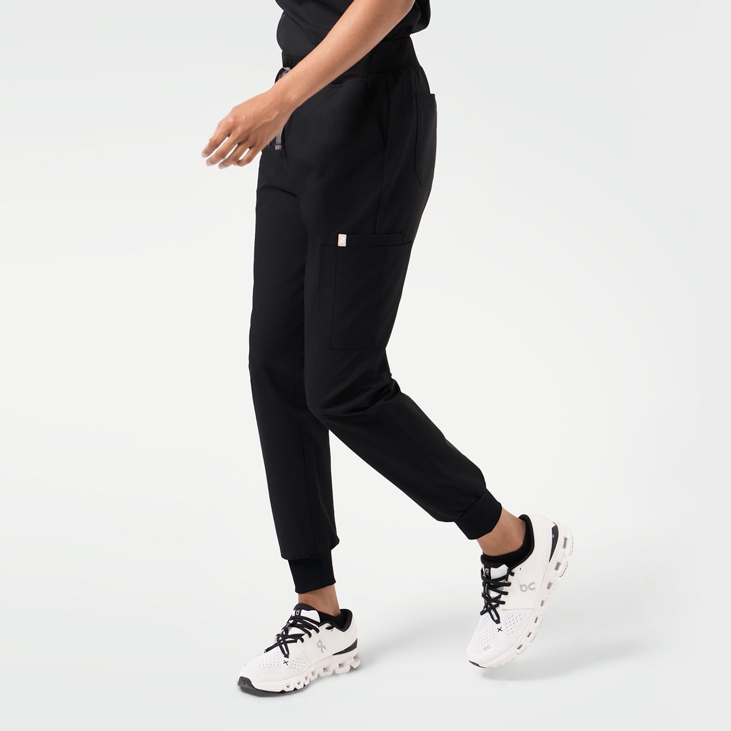 Model walking in Eco-Black jogger scrub pants with a side utility pocket and ribbed ankle cuffs.