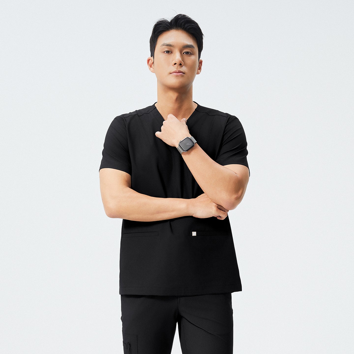 Man in black scrubs with a V-neck and double pockets, looking to the side with a thoughtful expression,Eco Black