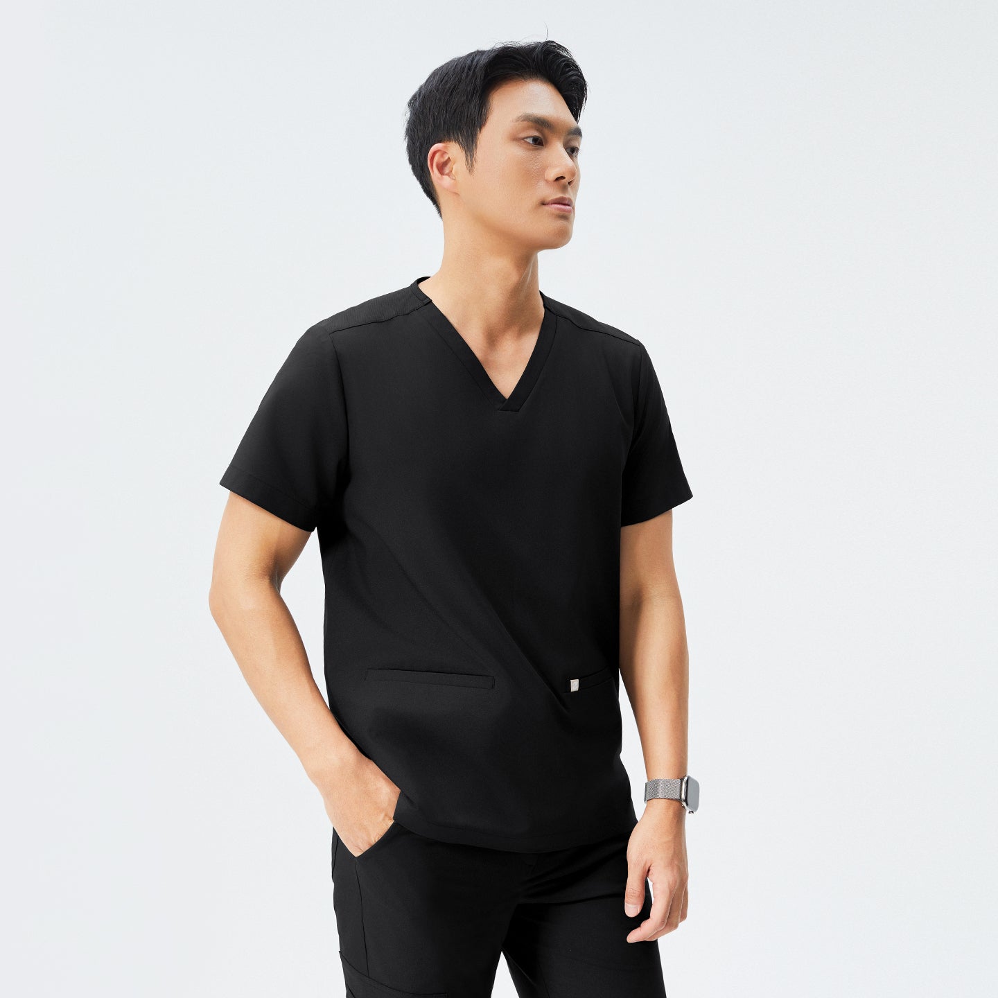 Man in black scrubs with a V-neck and double pockets, checking the time on his smartwatch,Eco Black