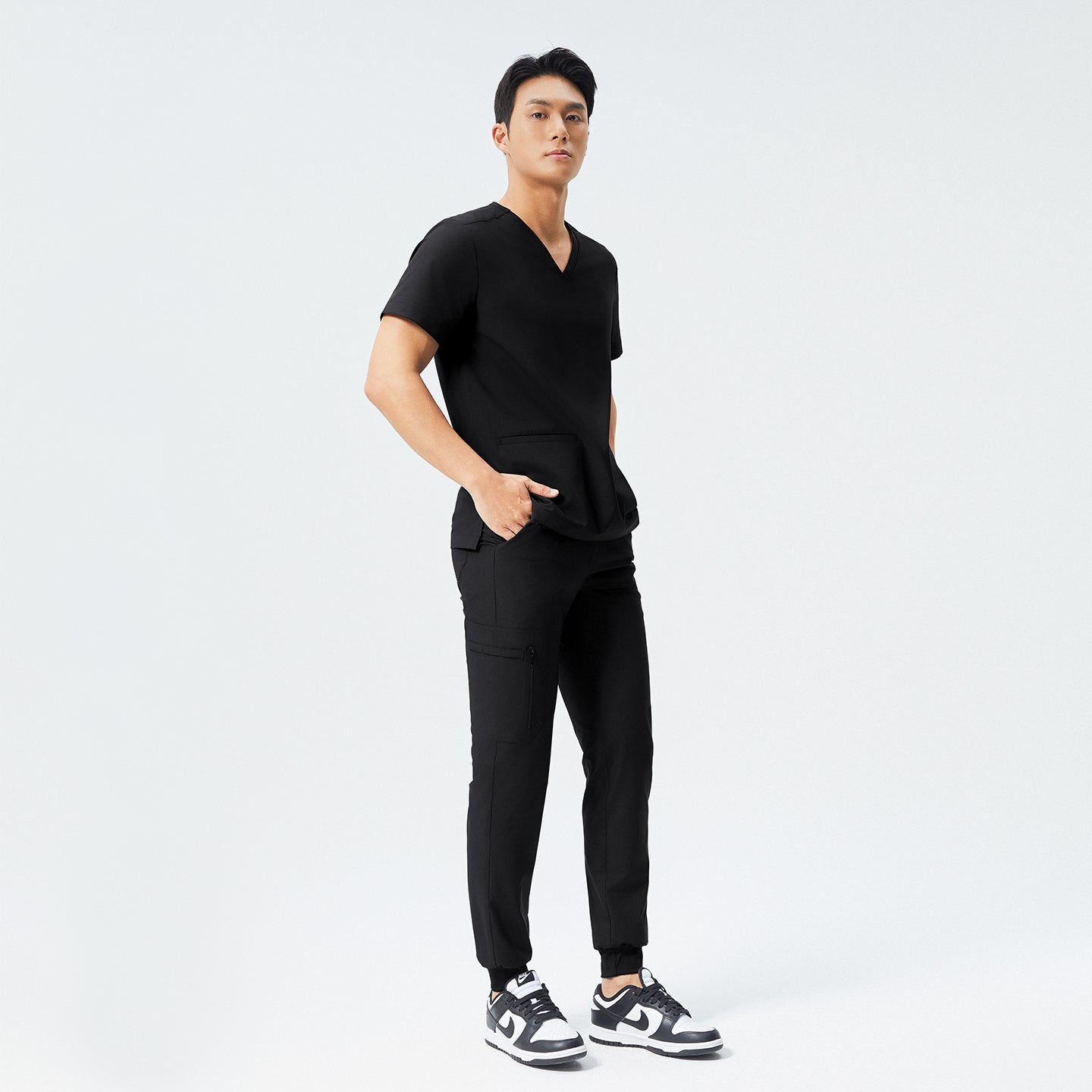 Eco Black scrub top with two pockets and matching eco black jogger scrub pants with hands in pocket and wearing matching black sneakers,Eco black