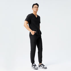 Image of Eco Black scrub top with two pockets and matching eco black jogger scrub pants with hands in pocket and wearing matching black sneakers,Eco black