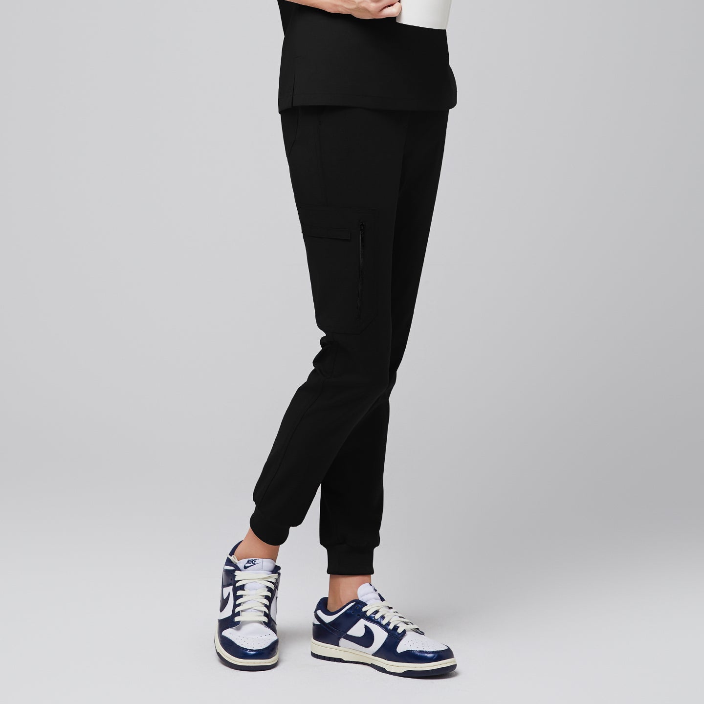 Image of Side view of eco black jogger scrub pants with zipper pocket and elastic cuffs, paired with navy sneakers,Eco Black