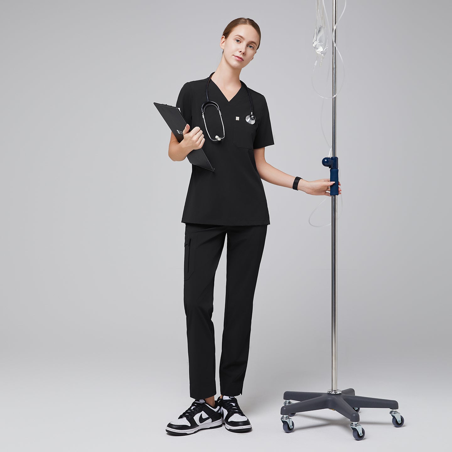 Healthcare professional wearing a coordinated scrub set with functional pockets and a split hem design, accessorized with a stethoscope and clipboard, standing confidently by medical equipment,Eco Black