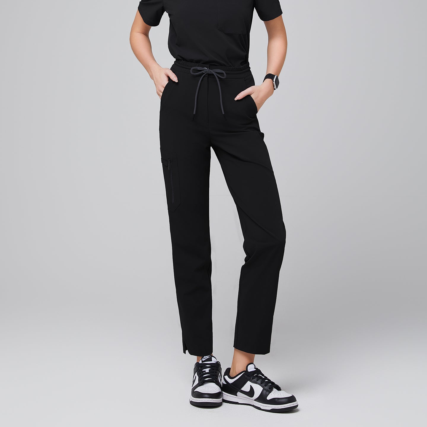 Image of Tailored scrub pants with a drawstring waist, a functional zipper pocket on the side, and split hem details, styled with athletic sneakers for a polished and practical appearance,Eco Black