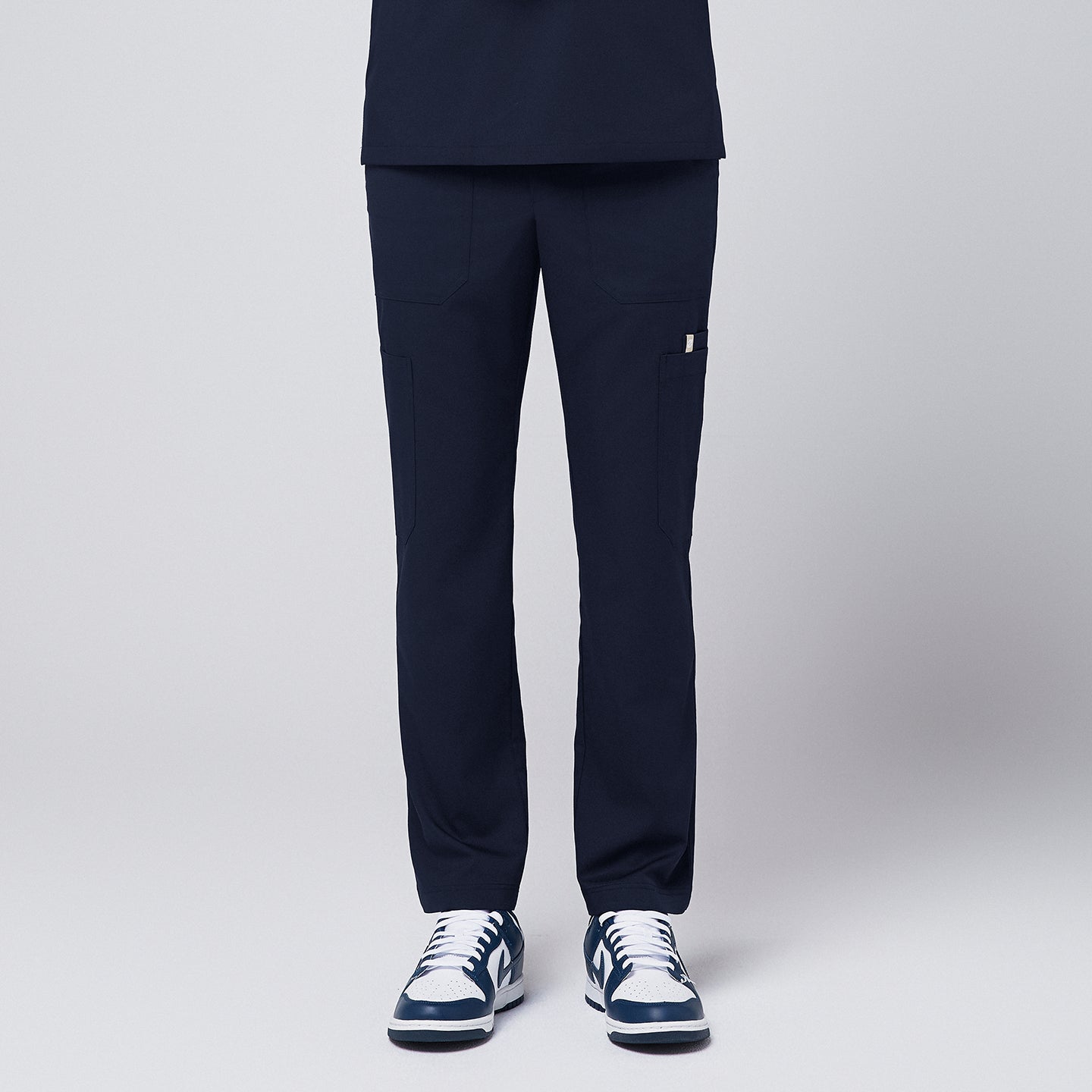 Image of Front view of navy straight scrub pants featuring multiple utility pockets, paired with navy and white sneakers,Eco Navy