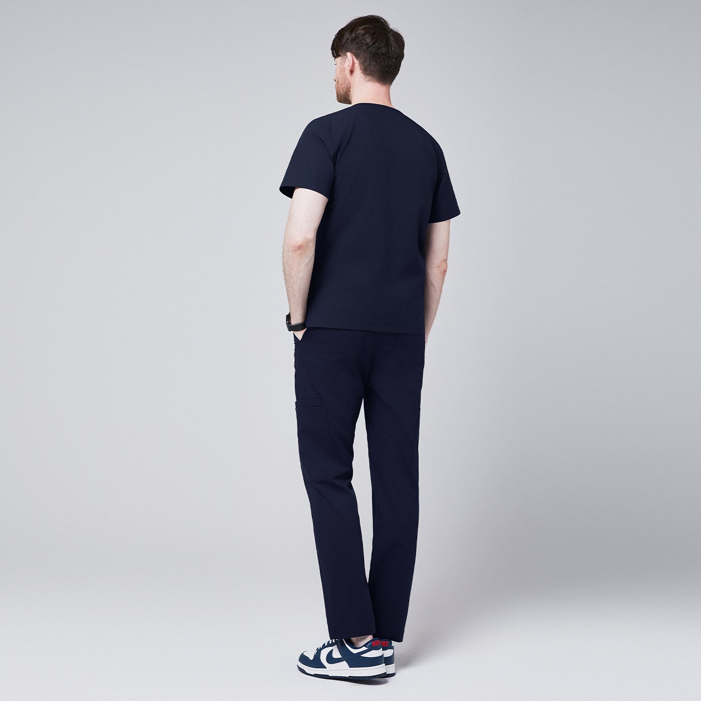 Image of Side-back view of a model wearing navy straight scrub pants and a matching top, paired with navy and white sneakers, showcasing a relaxed fit and utility pocket details,Eco Navy