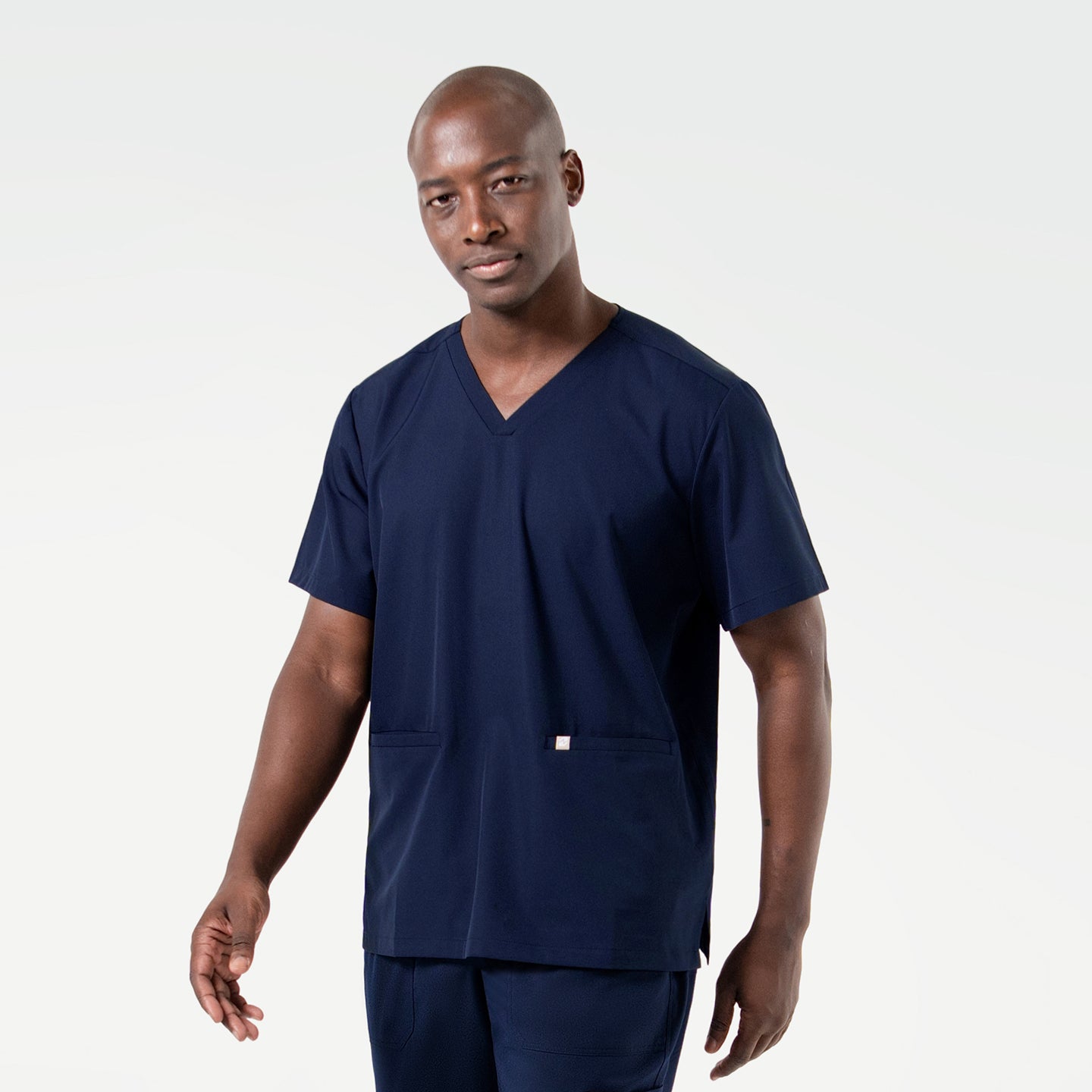 Wearing an Eco Navy scrub set, the male model stands with a composed expression and relaxed posture, highlighting the clean and professional design of the outfit.