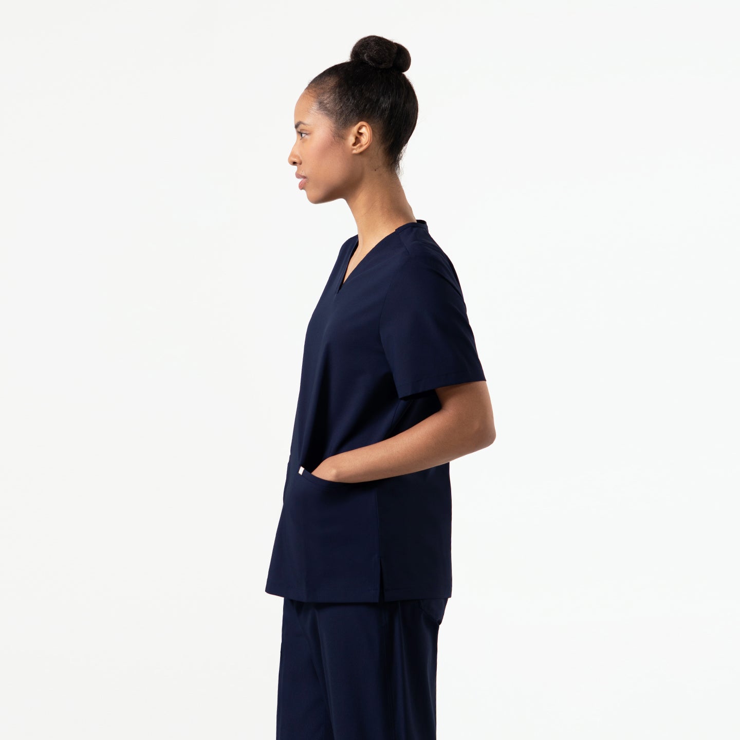 Image of Side view of a model wearing the Eco Navy Double Pocket Scrub Top with hands in pockets.