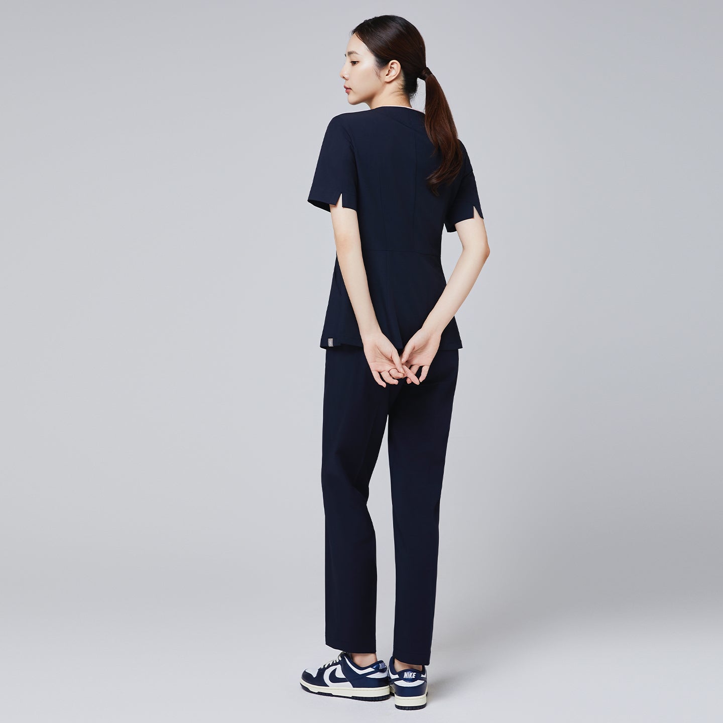Back view of eco navy scrub set with short-sleeve top and matching banding pants, paired with Nike navy and white sneakers,Eco Navy