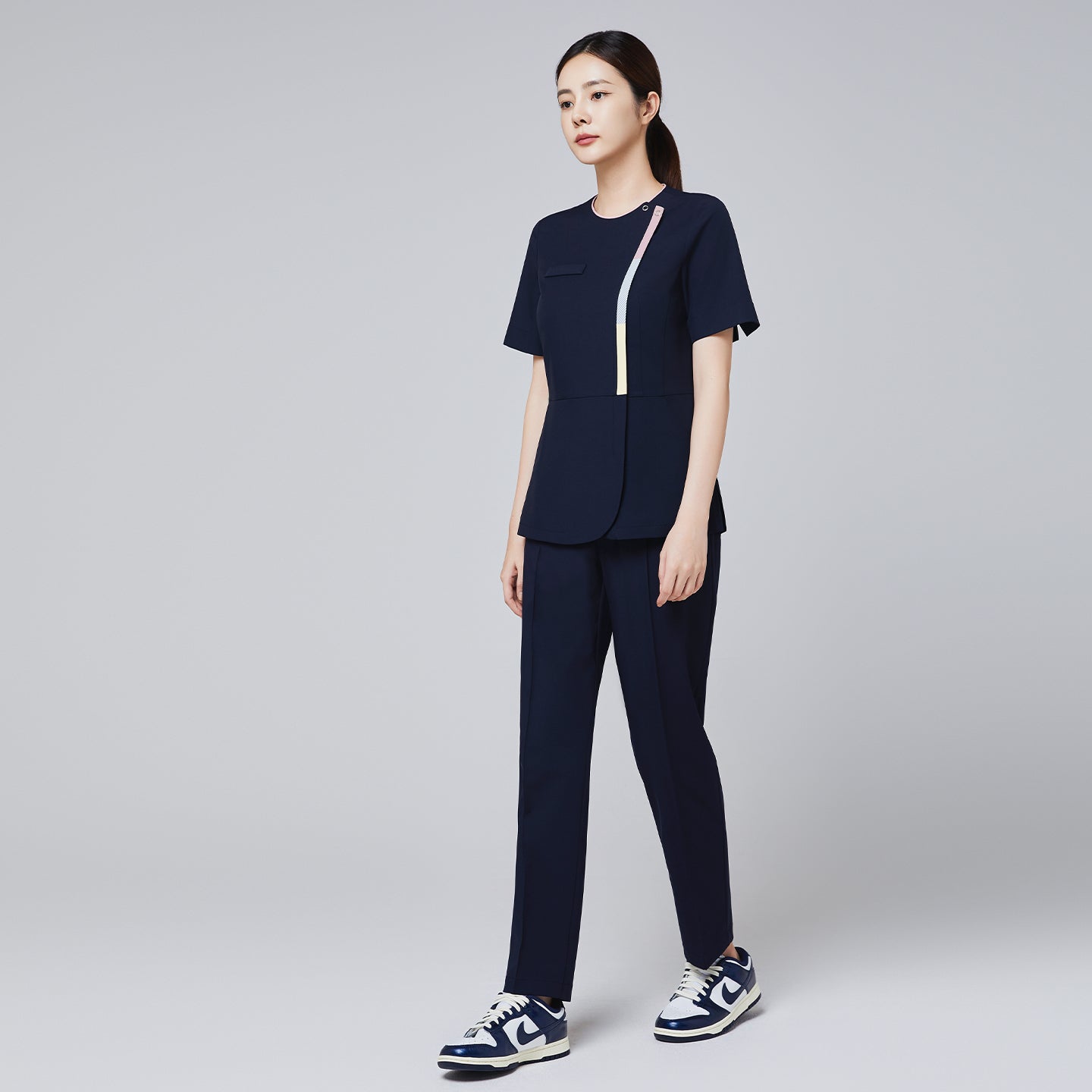 Image of Eco navy scrub set featuring a short-sleeve top with colorful stripe accents and matching banding pants, styled with navy and white sneakers,Eco Navy