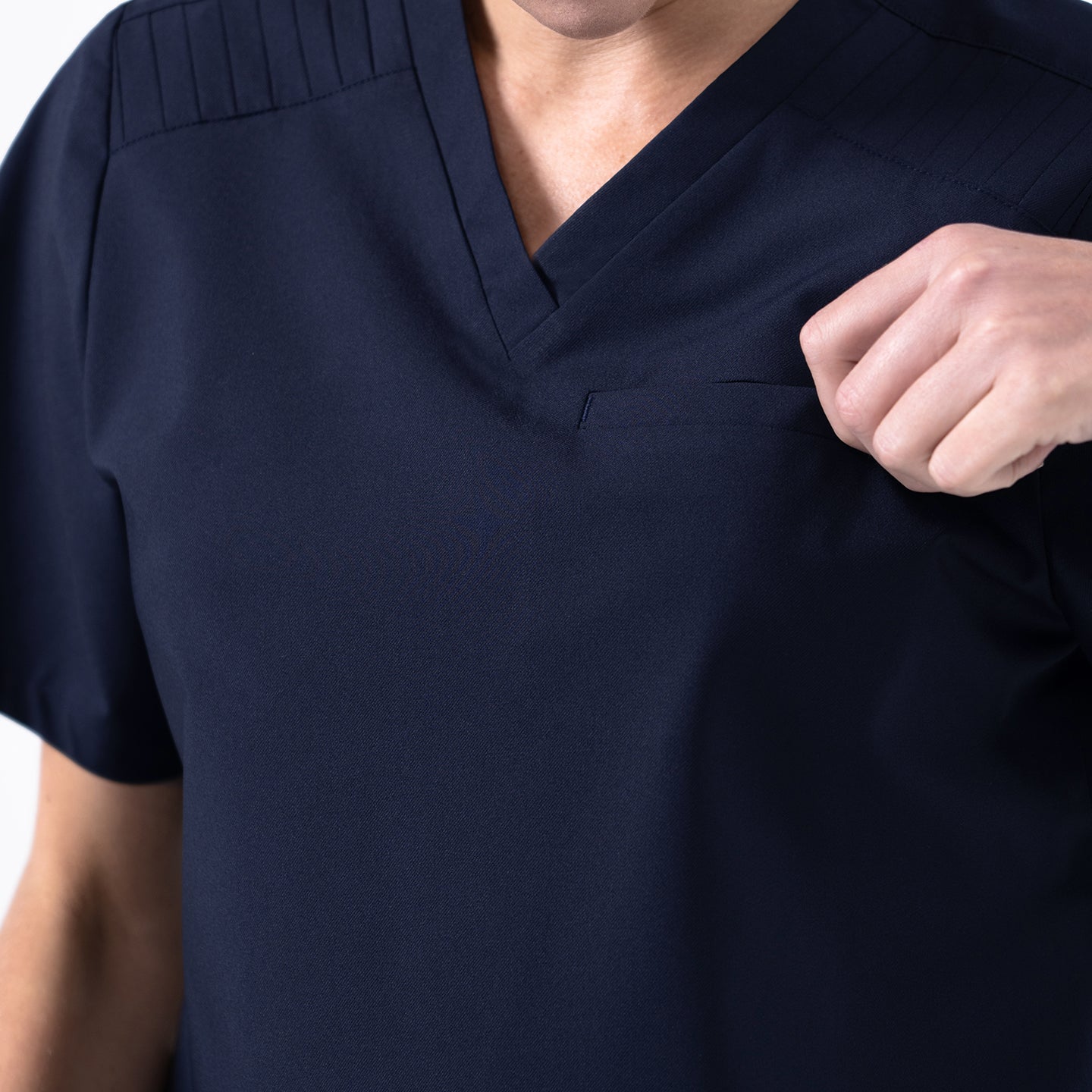 Image of Close-up of the Eco-Navy pleated-shoulder scrub top, highlighting the stitched shoulder detailing and the subtle chest pocket as the model adjusts the fabric.