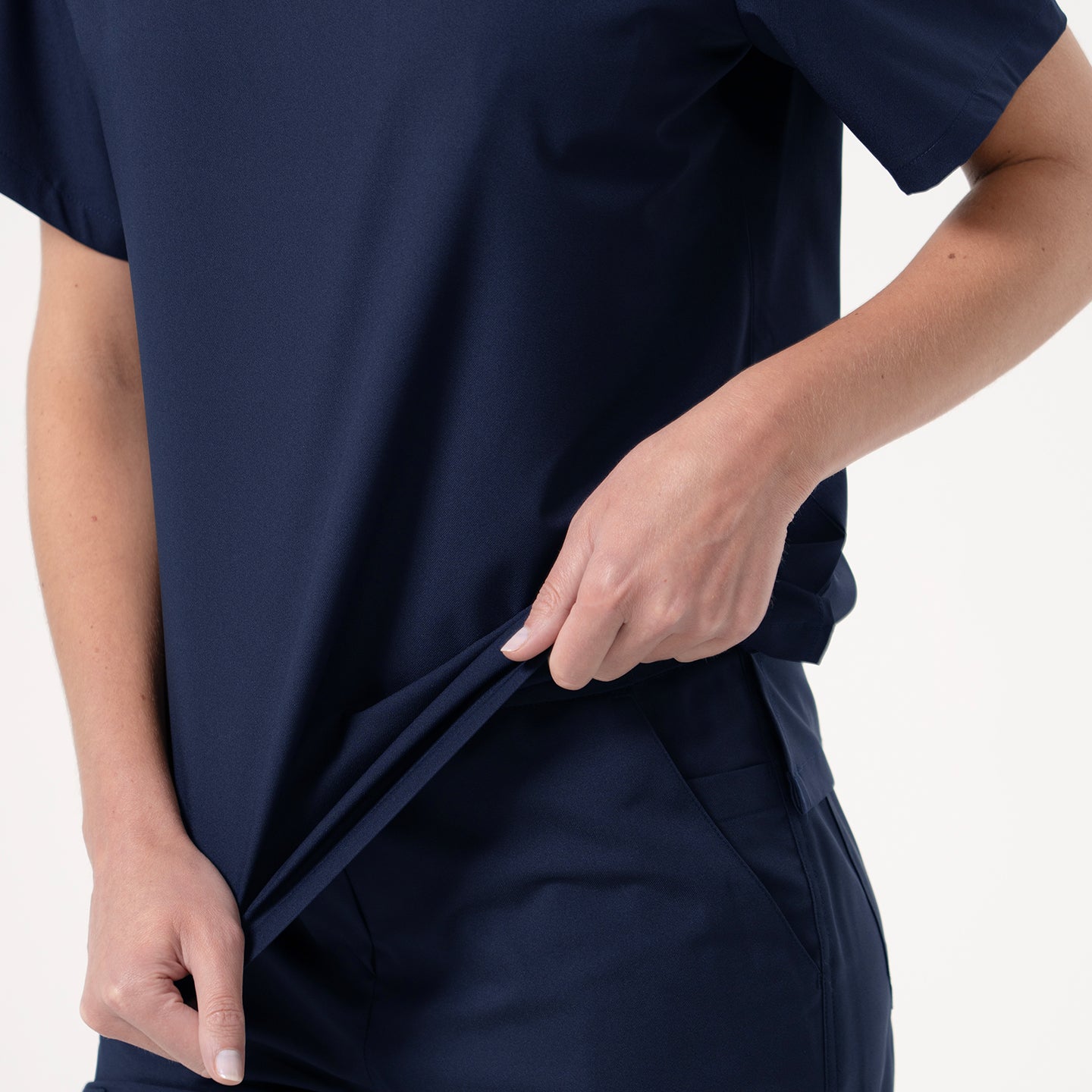 Image of Detail shot of Zenir’s Eco-Navy pleated-shoulder scrub top paired with matching pants, with the model pulling the side of the shirt to emphasize its soft stretch and comfortable fit.