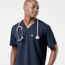 Image of Wearing an Eco Navy scrub top, the male model looks to the side with a light pink stethoscope draped around his neck.