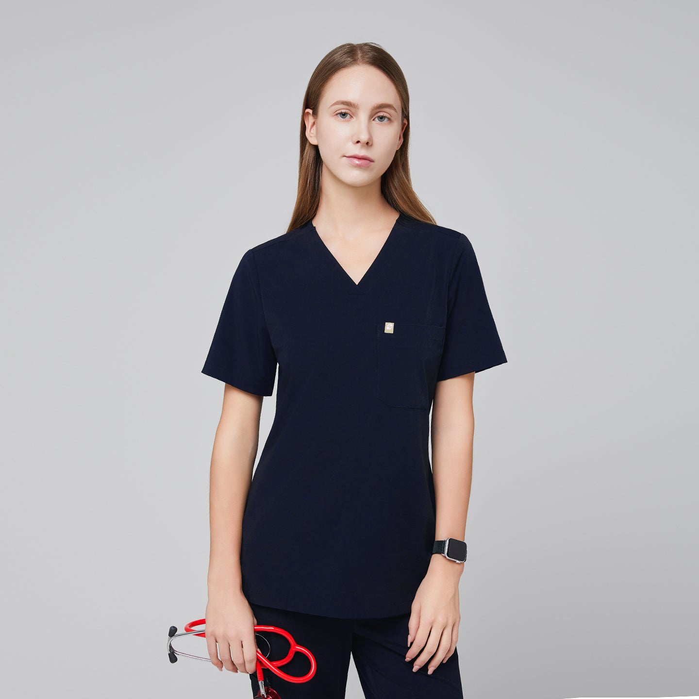 Image of Navy scrub top with single pocket paired with matching scrub pants, holding a red stethoscope with a watch,Eco navy