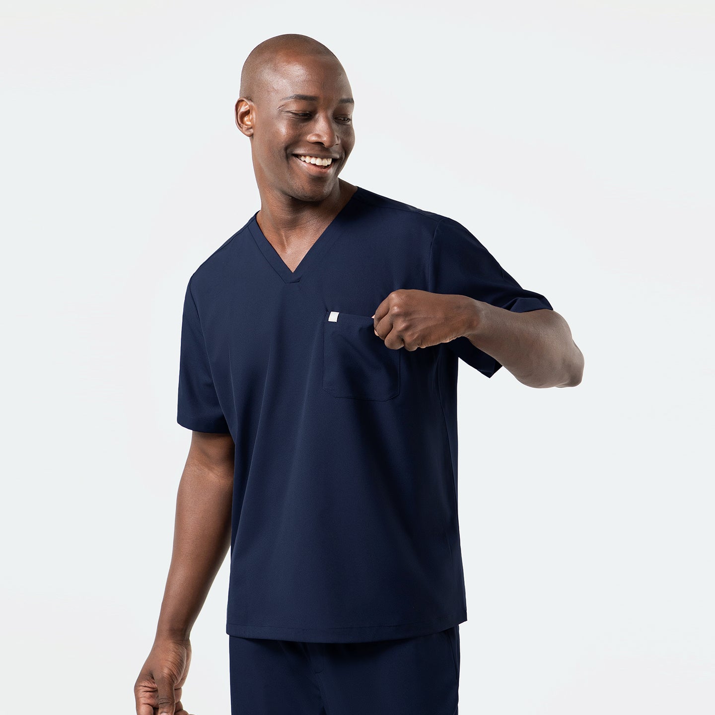 Image of In this front-facing shot, the Eco-Navy single-pocket scrub top displays its simple one-pocket layout, polished V-neckline, and sleek, breathable fabric as the wearer casually interacts with the pocket.
