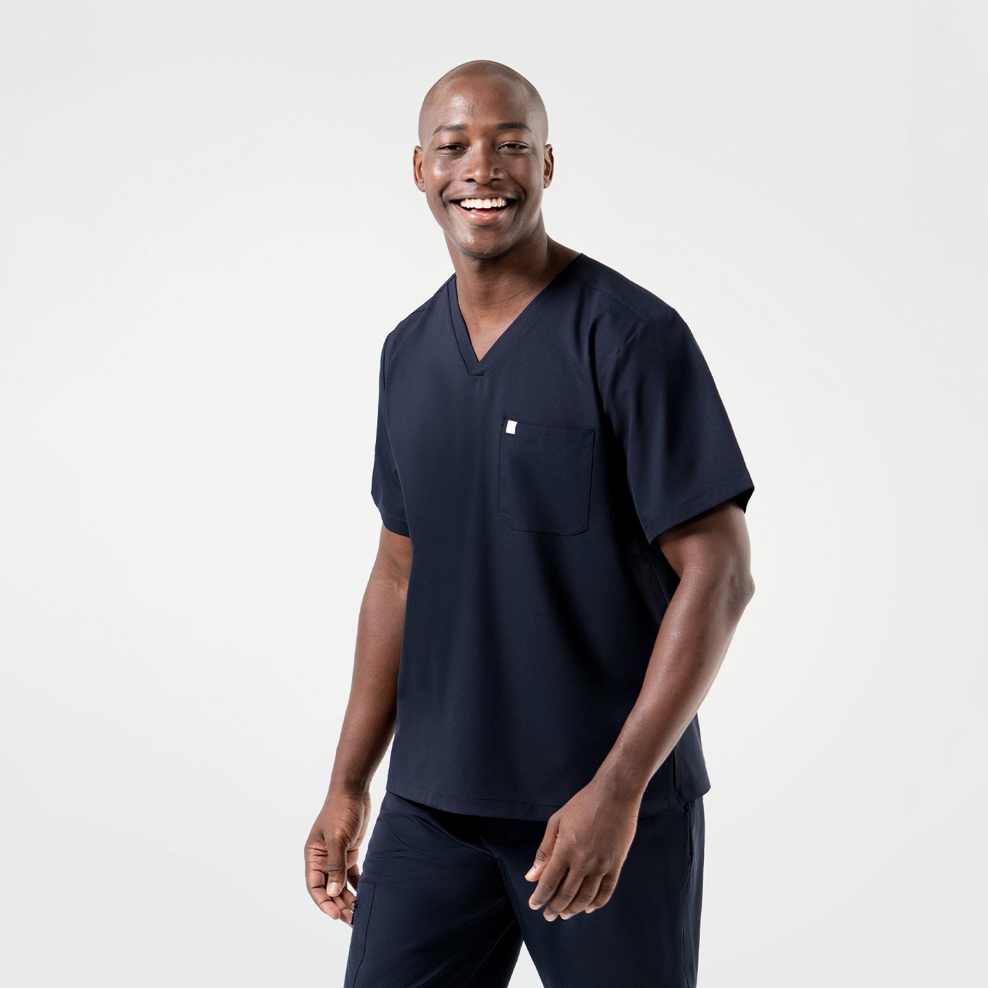 Smiling warmly, the model takes a step ahead in the Eco Navy Single Pocket Scrub Top, arms moving gently with the rhythm of his walk.