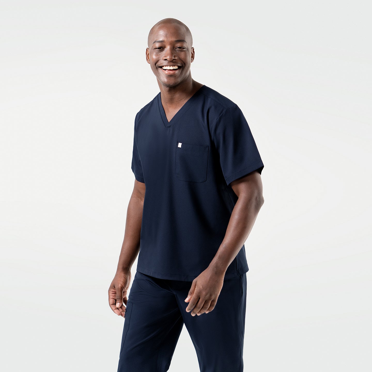 Image of Smiling warmly, the model takes a step ahead in the Eco Navy Single Pocket Scrub Top, arms moving gently with the rhythm of his walk.