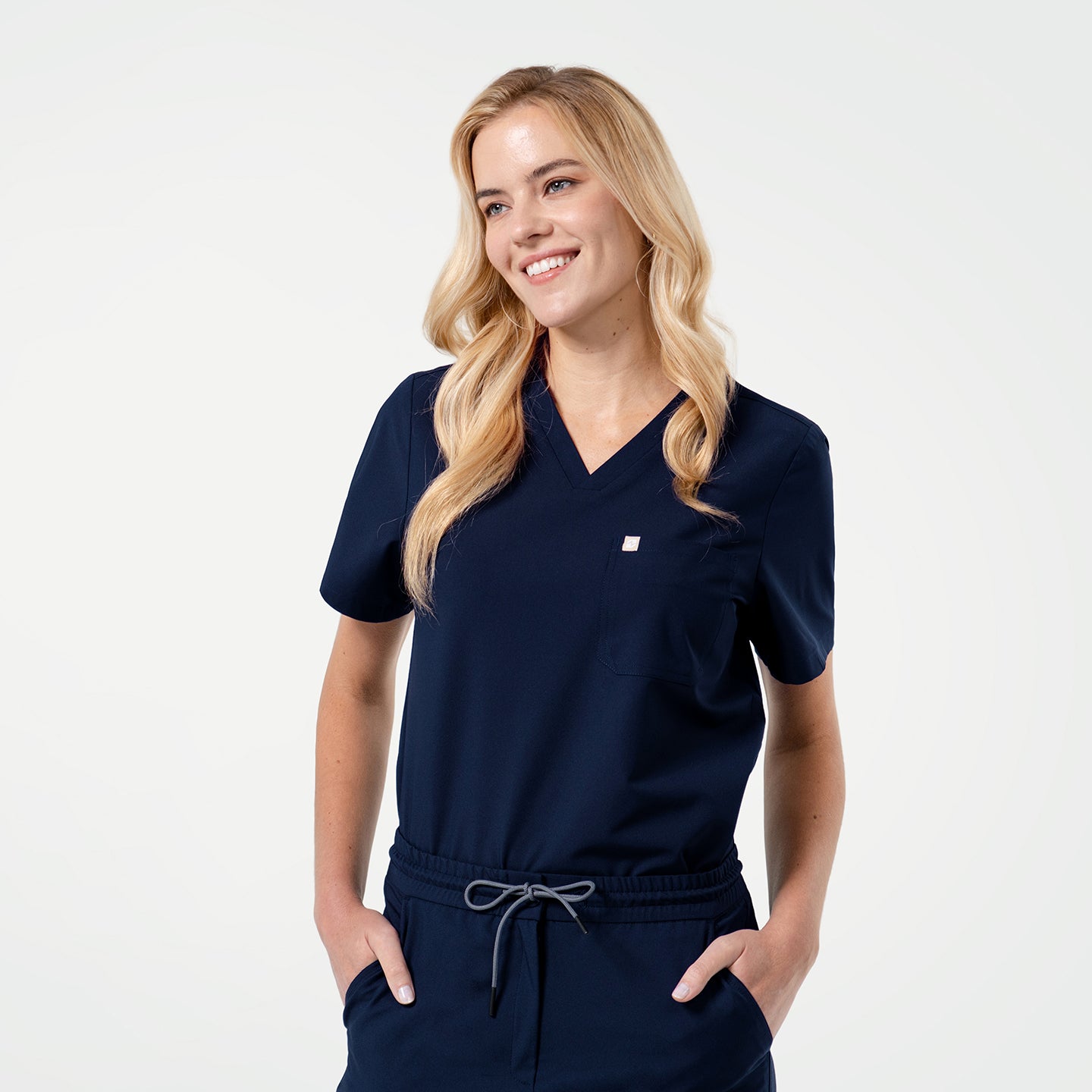 Smiling model wearing an Eco Navy scrub top with a single pocket, posing with hands in pockets.