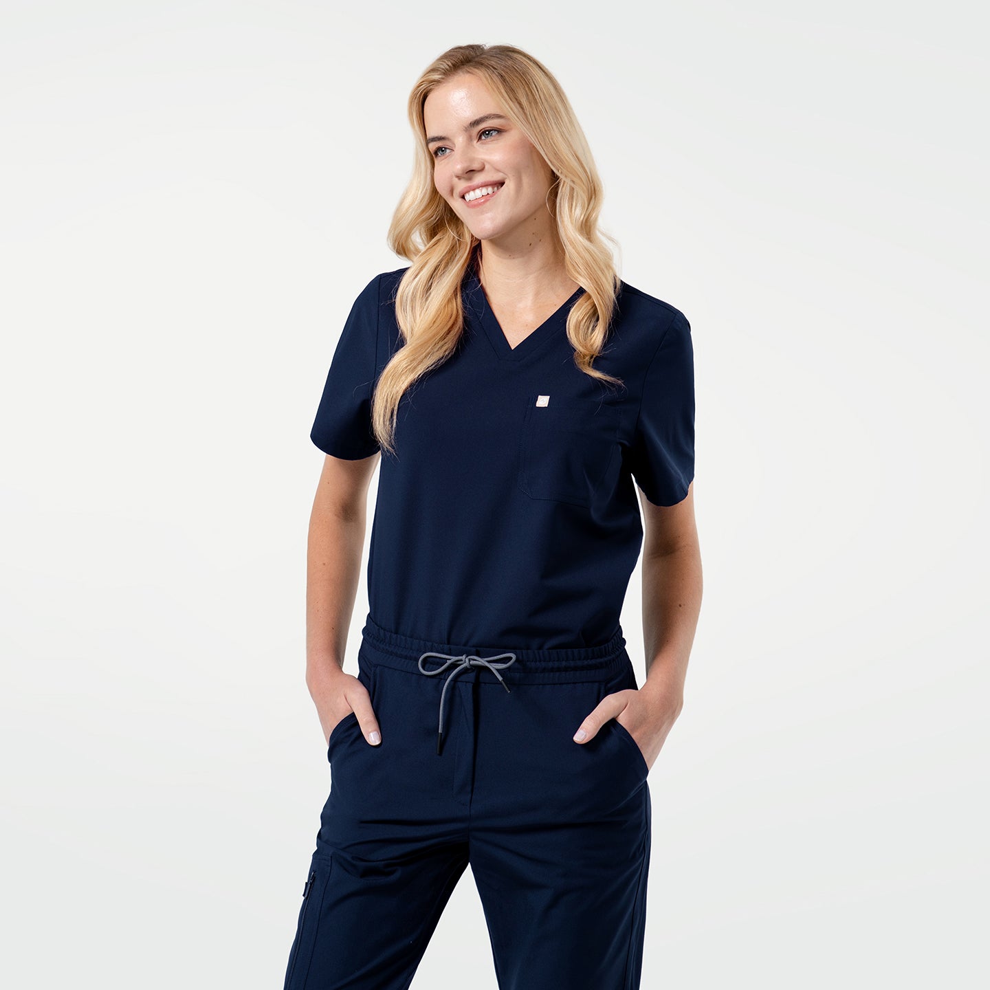 Image of Smiling model wearing an Eco Navy scrub top with a single pocket, posing with hands in pockets.